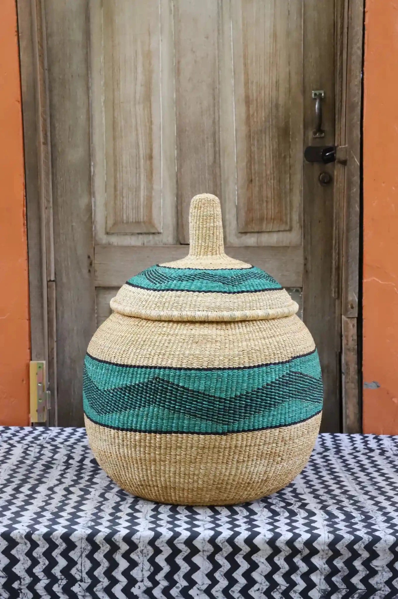 Woven storage basket with colorful patterns on a black and white cloth against a wooden door