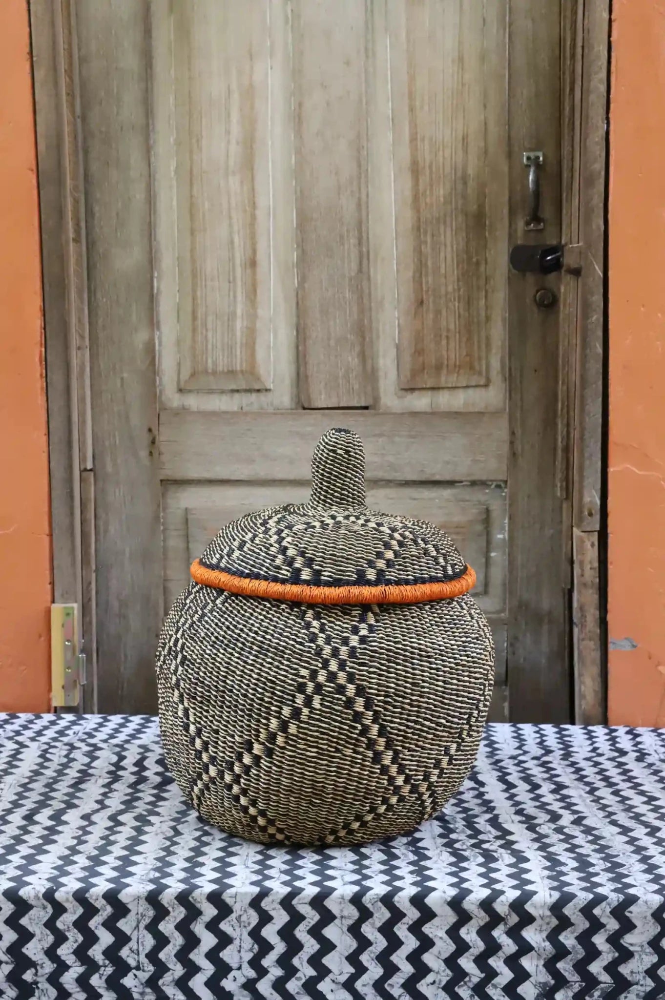 Woven storage basket with colorful patterns on a black and white cloth against a wooden door