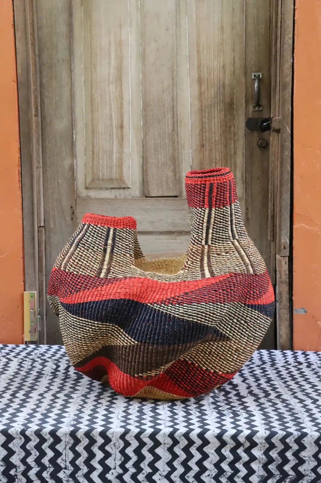 A colorful, handwoven piece sitting on a black and white cloth against a wooden door