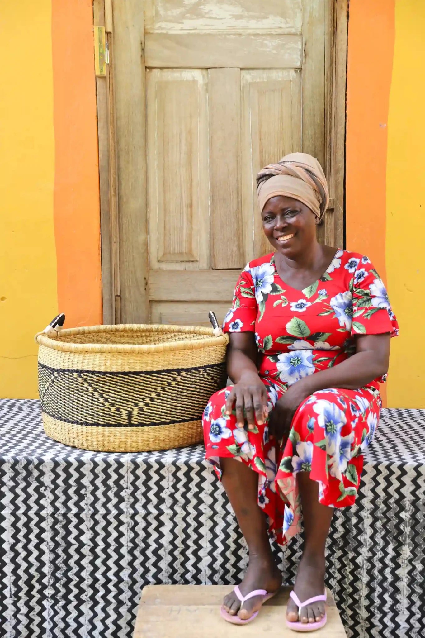 Woven Tub (Large) with woman weaver handwoven in Ghana sitting on black and white cloth and wooden door in background
