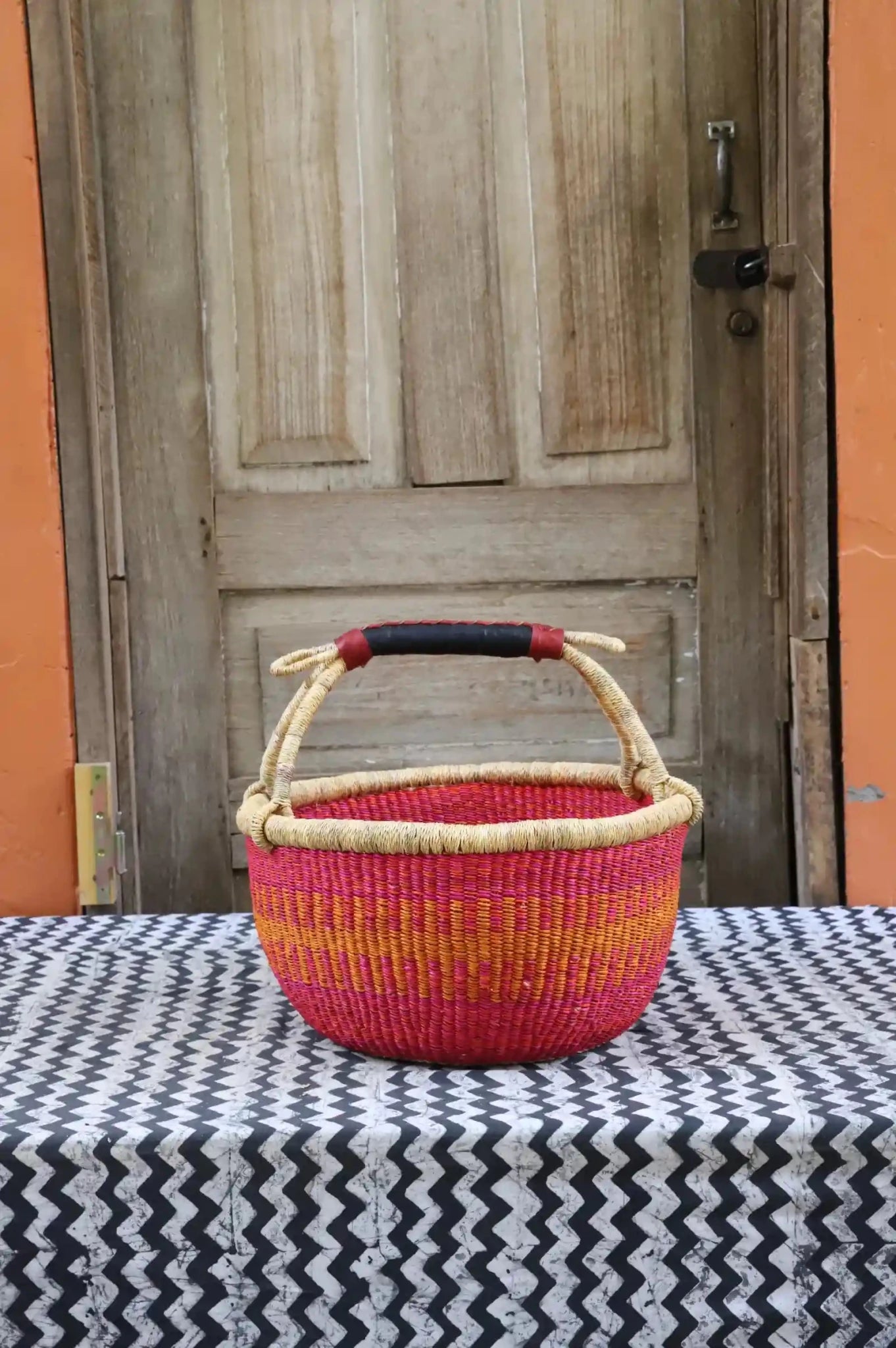 Woven carry on bag with premium leather handles on a black and white cloth against a wooden door.