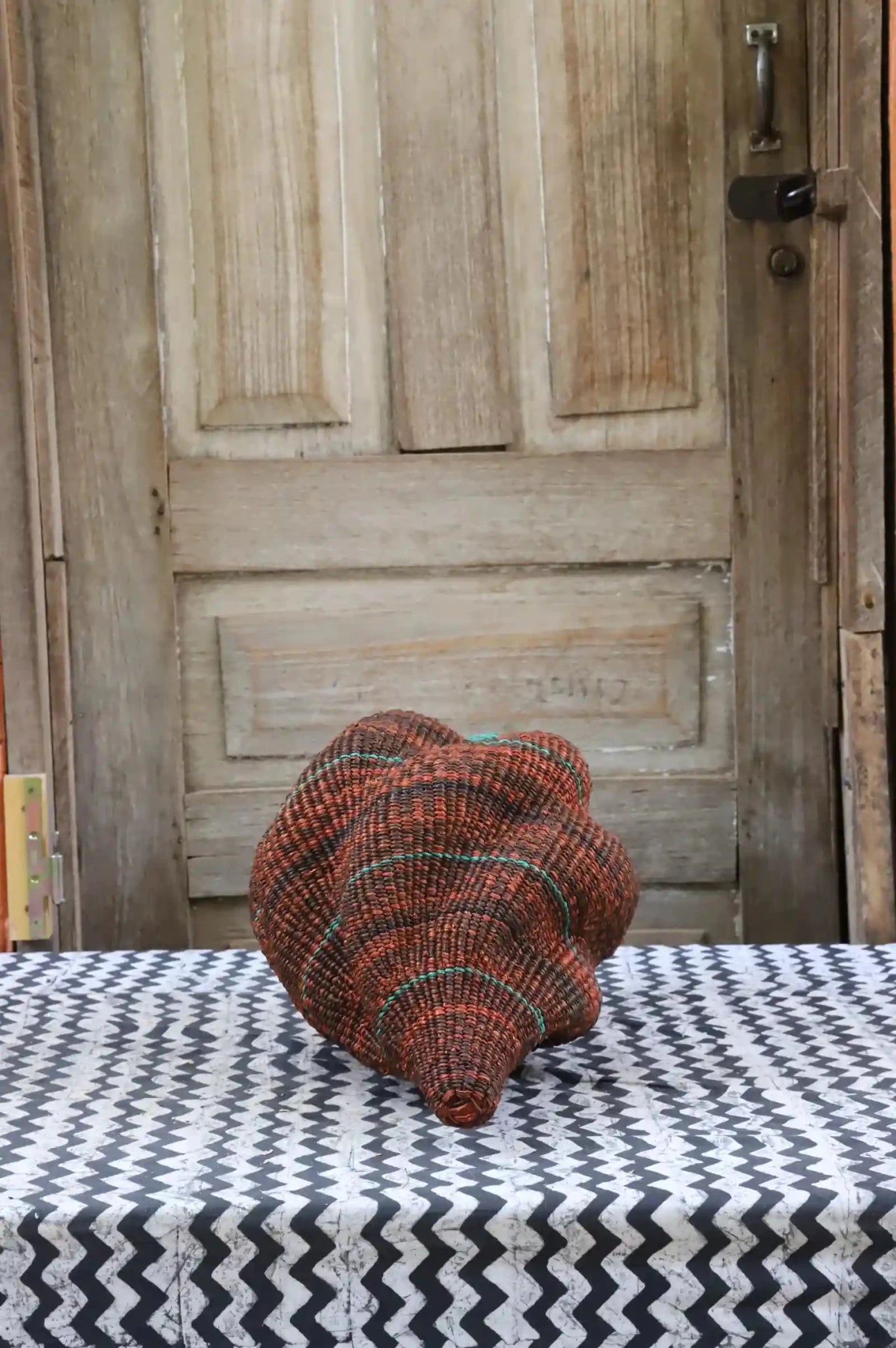 Colorful conch-shaped woven piece on a black and white cloth against a wooden door.