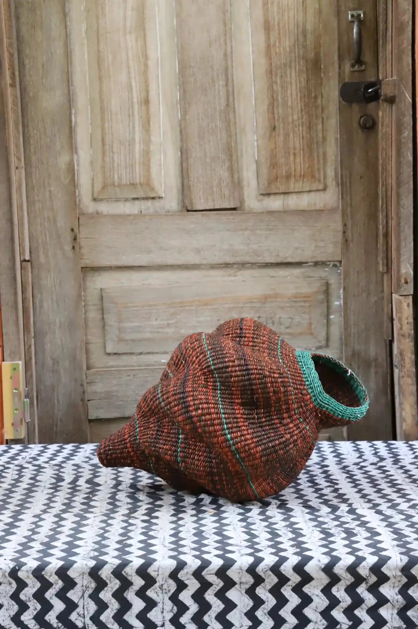 Colorful conch-shaped woven piece on a black and white cloth against a wooden door.