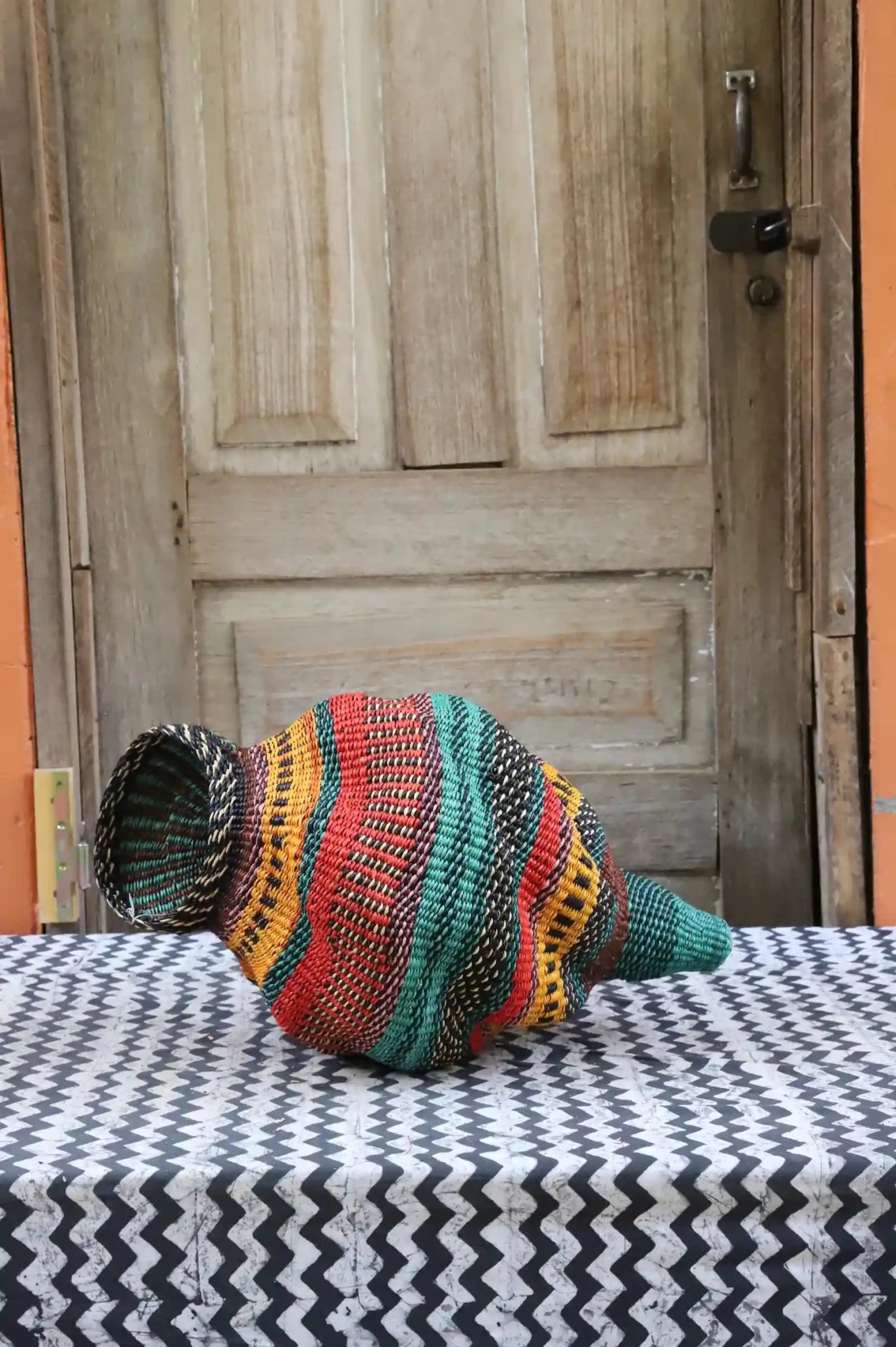Colorful conch-shaped piece on a black and white cloth against a wooden door.