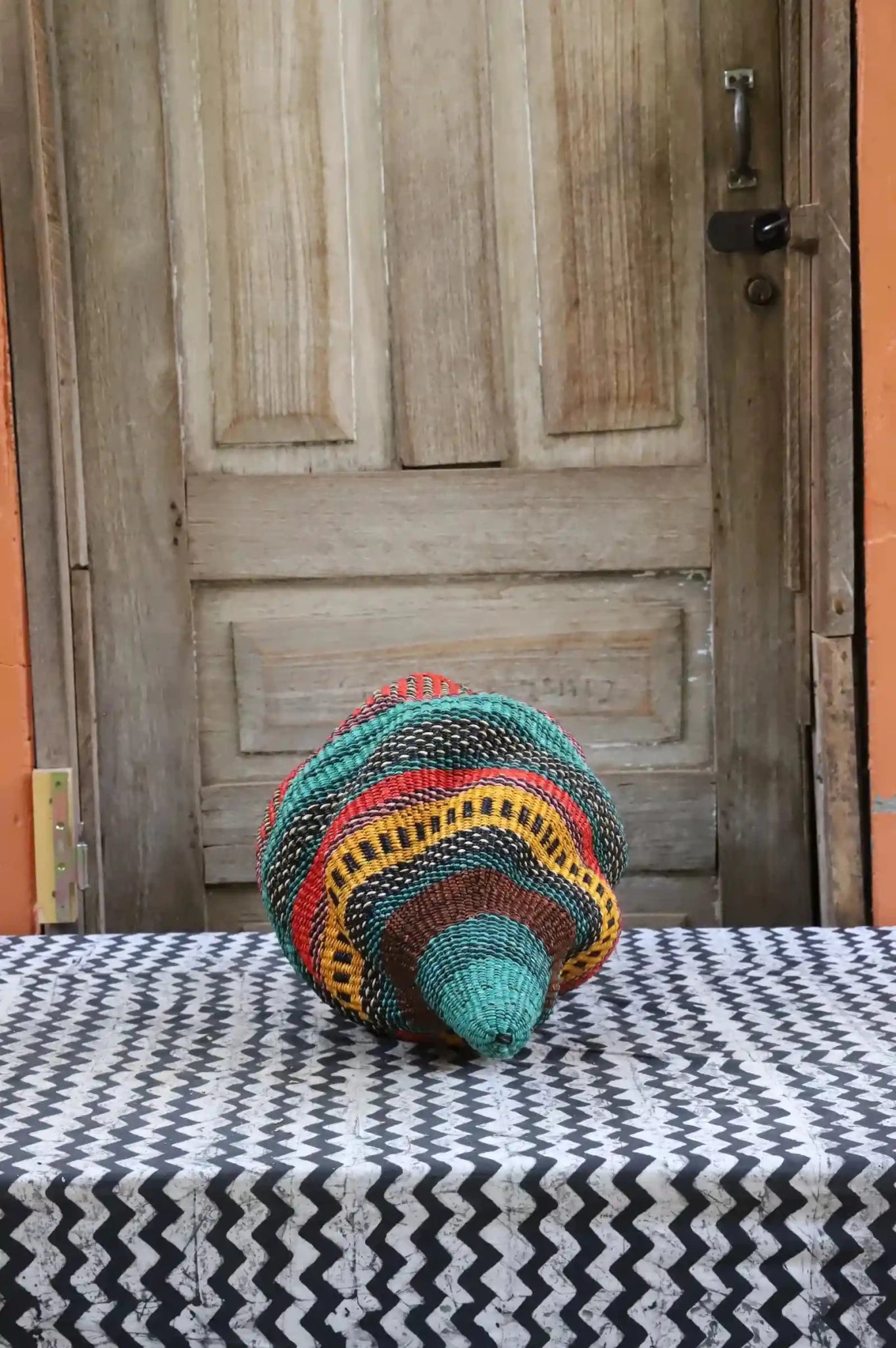 Colorful conch-shaped woven piece on a black and white cloth against a wooden door.