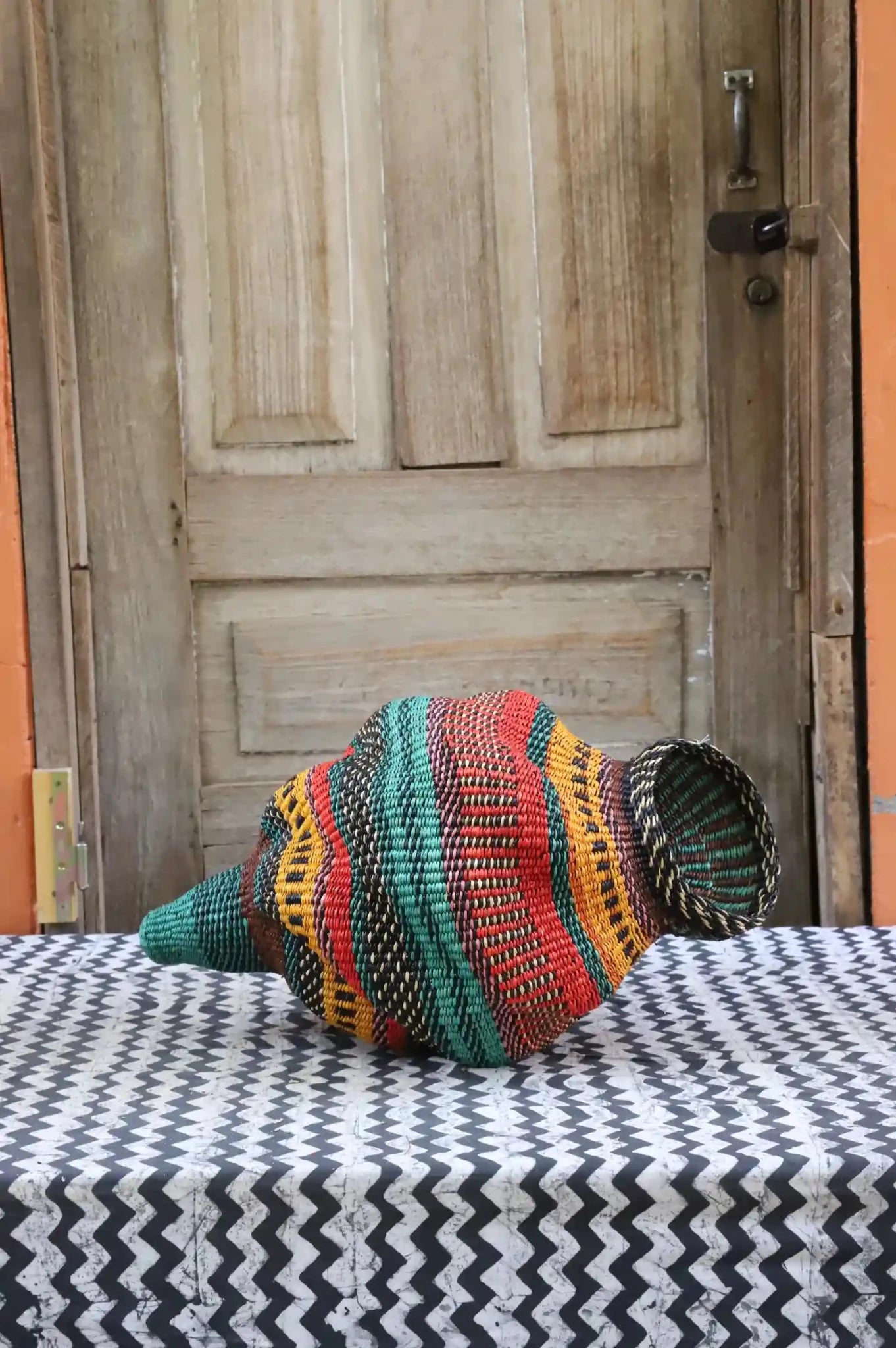 Colorful conch-shaped woven piece on a black and white cloth against a wooden door.