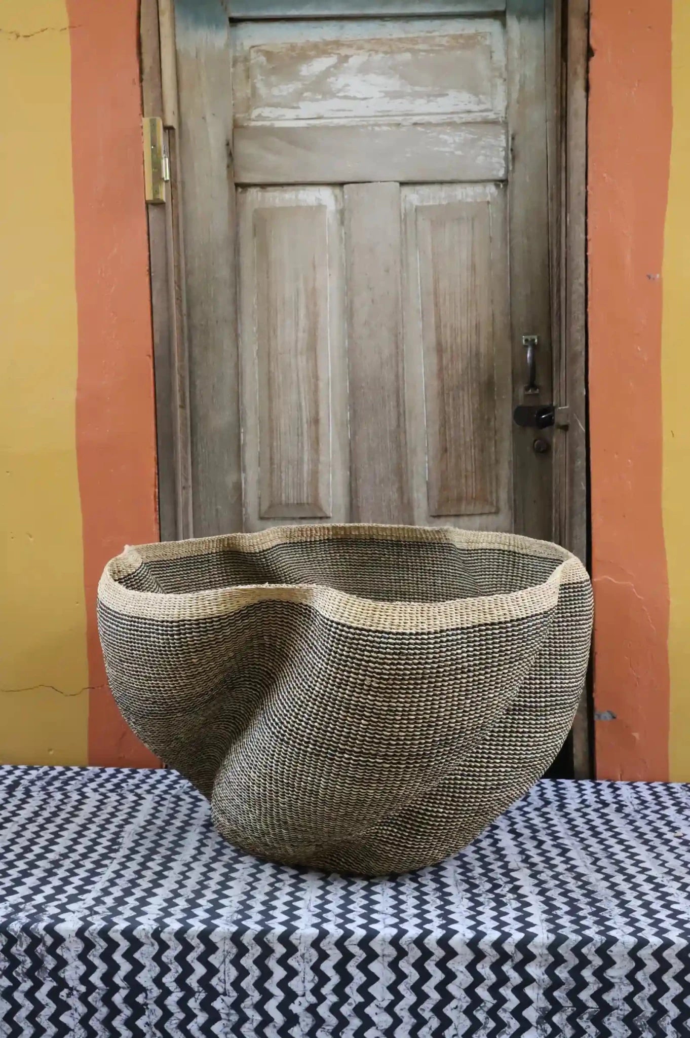 Patterned woven décor basket on a black and white cloth with a wooden door in the background.