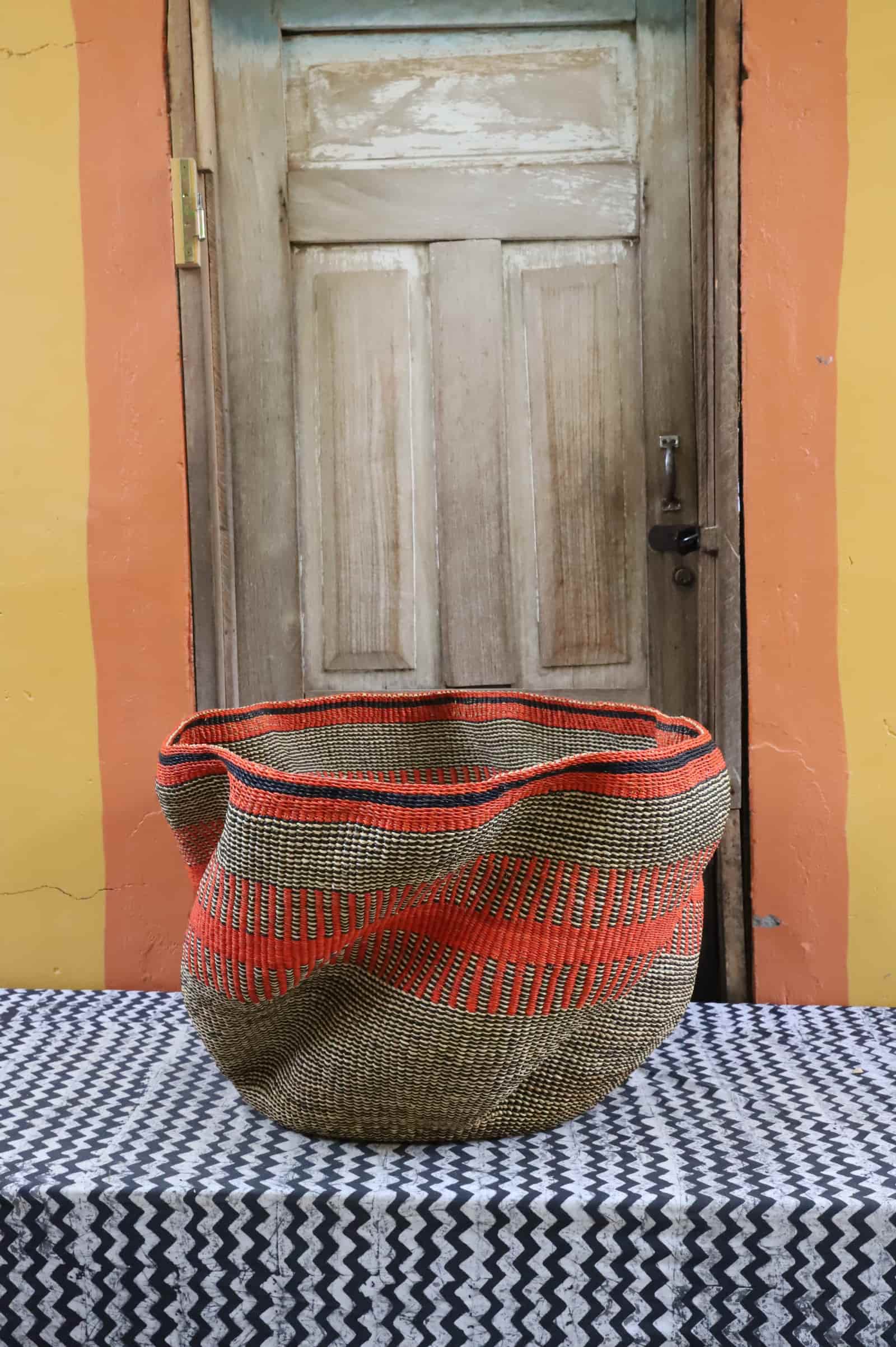 Large woven basket with geometric pattern on a black and white checkered tablecloth in front of a wooden door.
