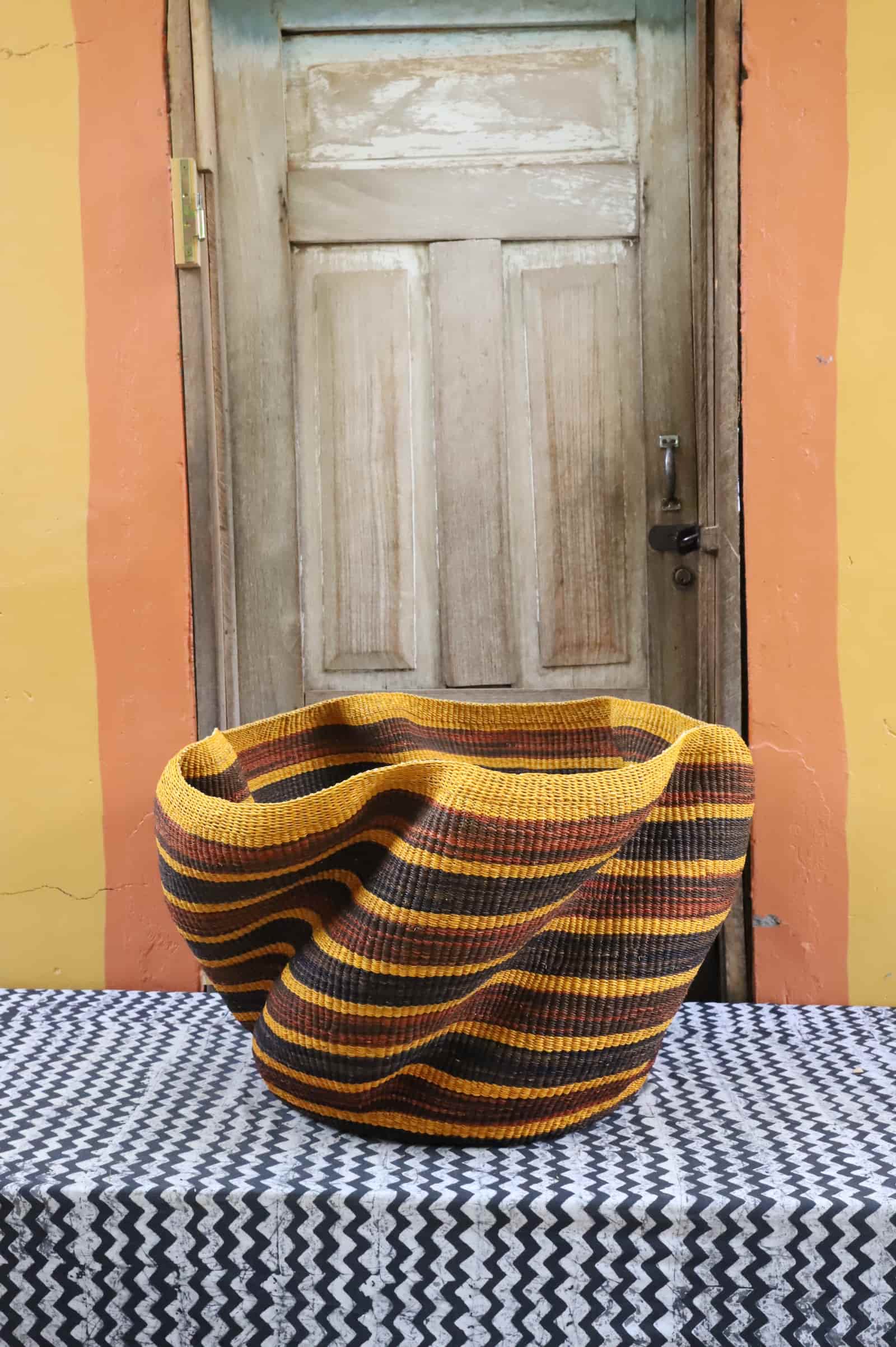Large woven basket with geometric pattern on a black and white checkered tablecloth in front of a wooden door.