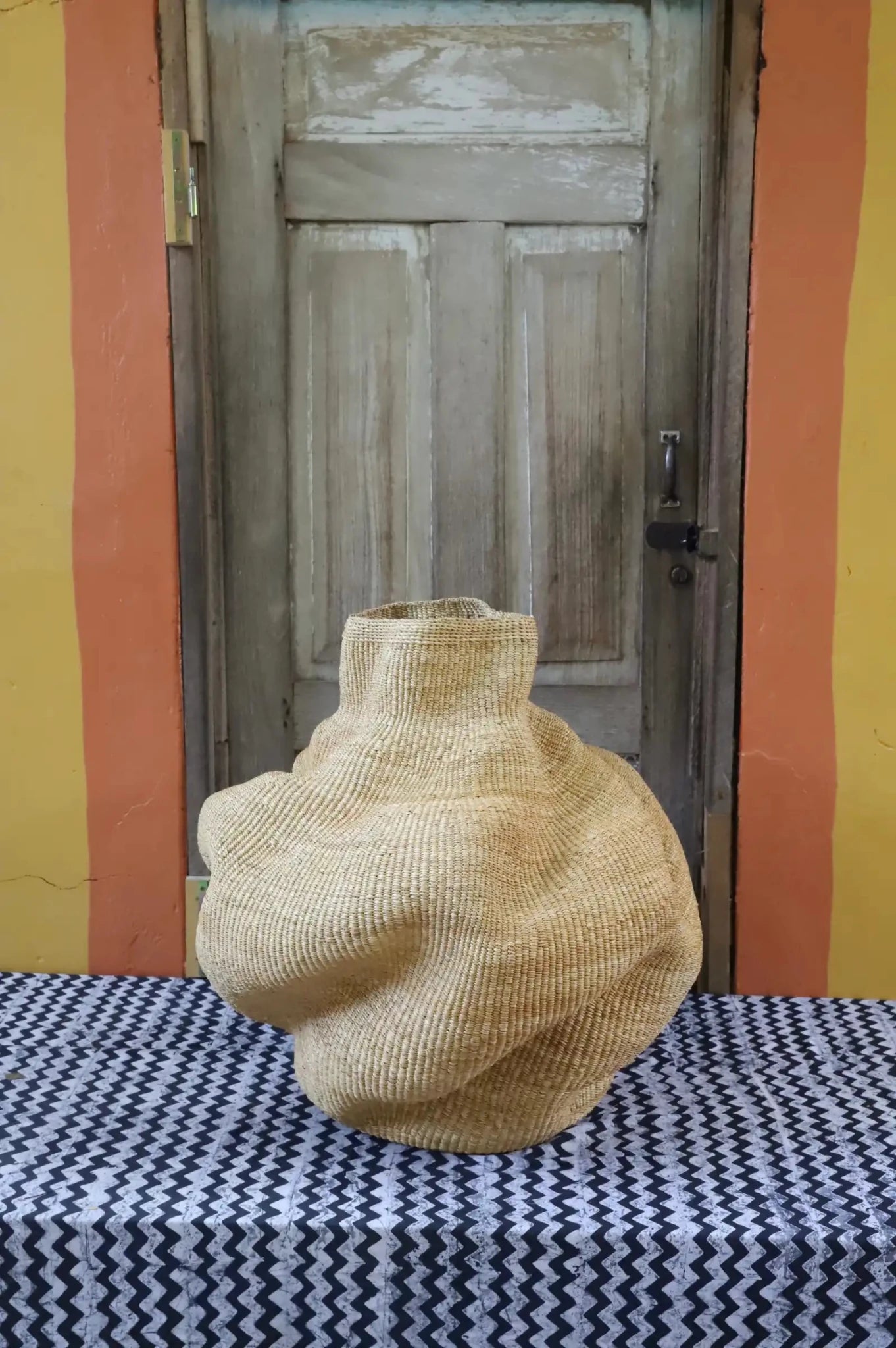 A handwoven piece with decorative curves sitting on a black and white cloth against a wooden door