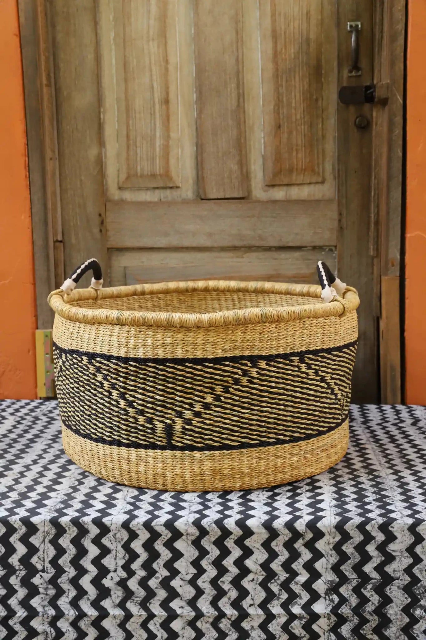 Woven Tub (Large) handwoven in Ghana sitting on black and white cloth with wooden door background

