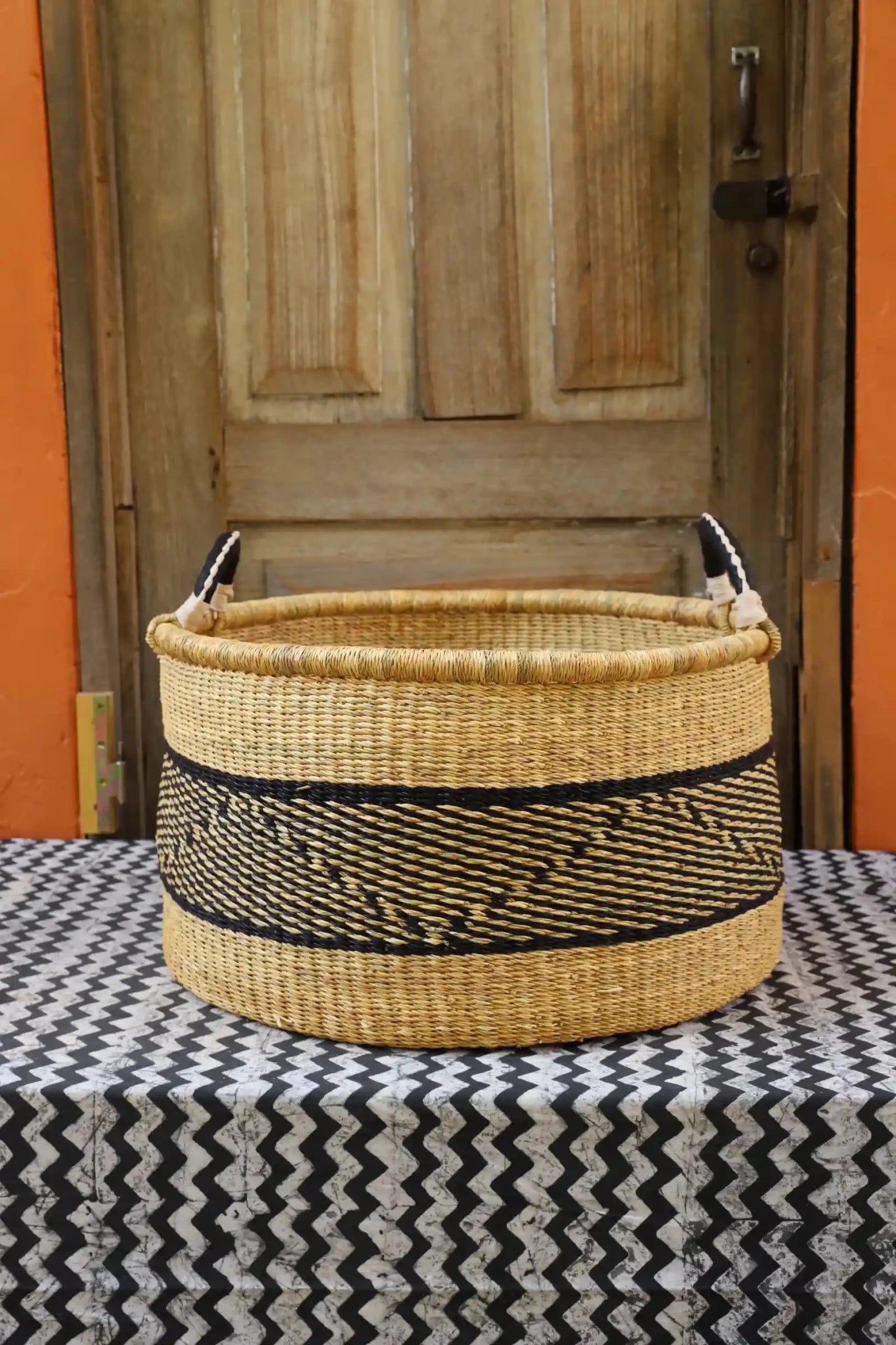 Woven Tub (Large) handwoven in Ghana sitting on black and white cloth with wooden door background
