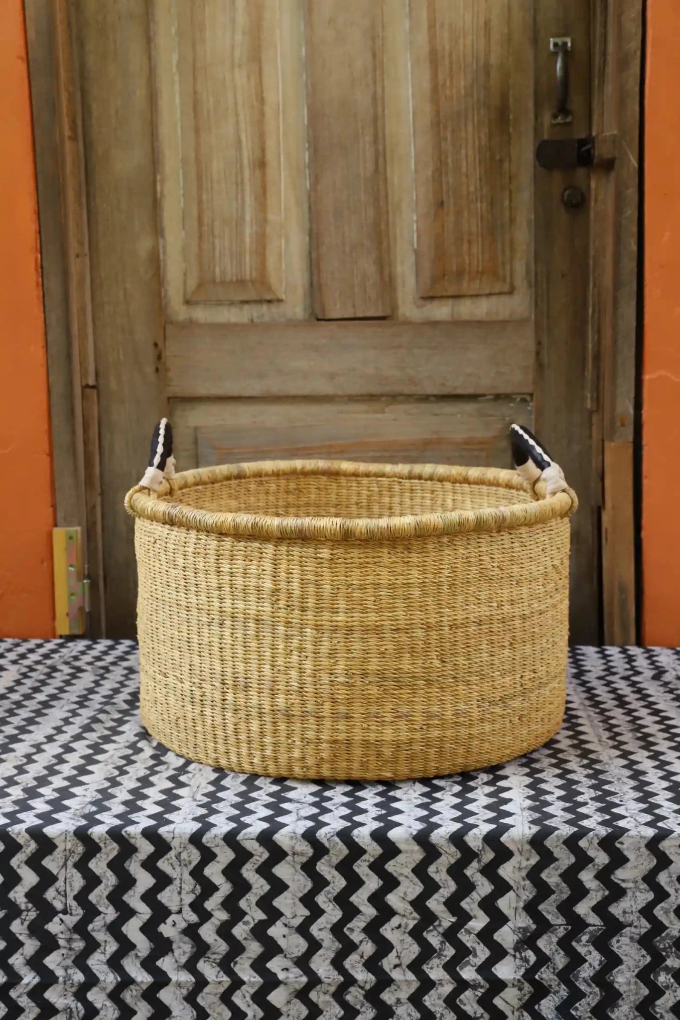 Woven Tub (Medium) handwoven in Ghana sitting on black and white cloth with wooden door background
