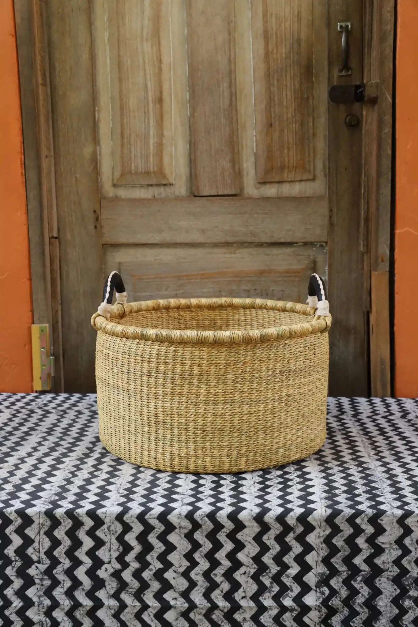 Woven Tub (Small) handwoven in Ghana sitting on black and white cloth with wooden door background
