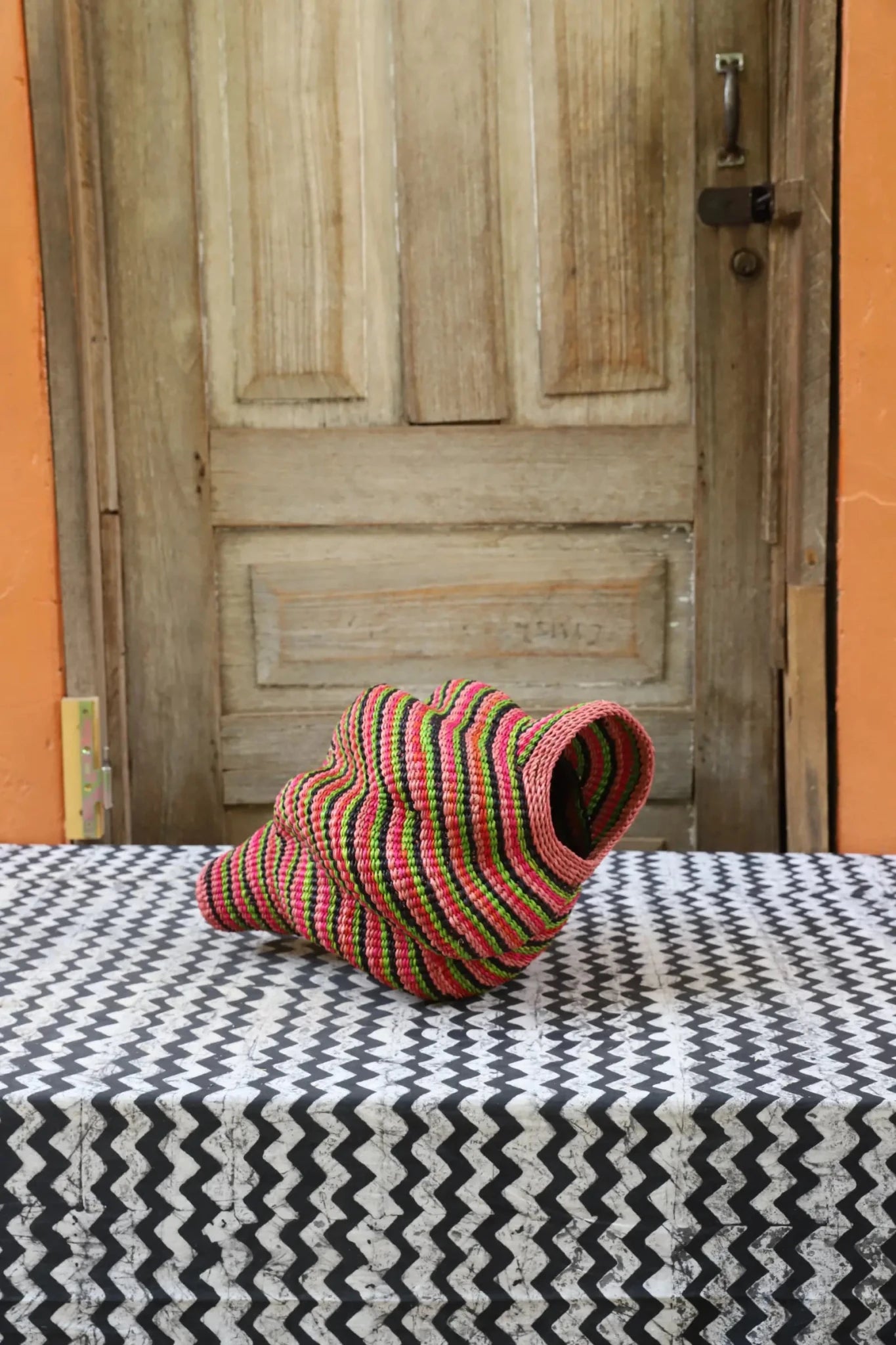 Woven conch piece on a black and white patterned surface with a wooden door in the background.