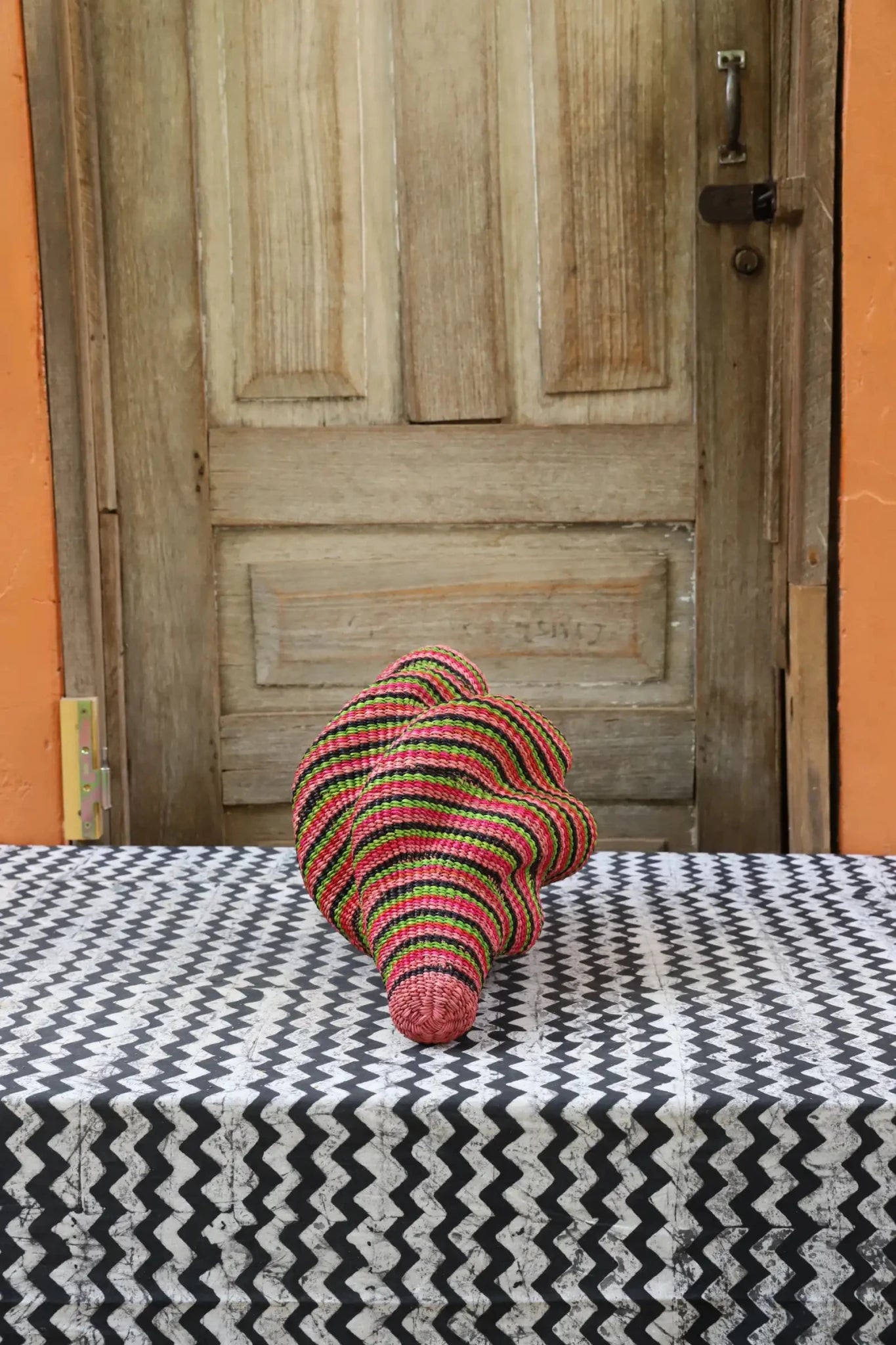 Woven conch piece on a black and white patterned surface with a wooden door in the background.