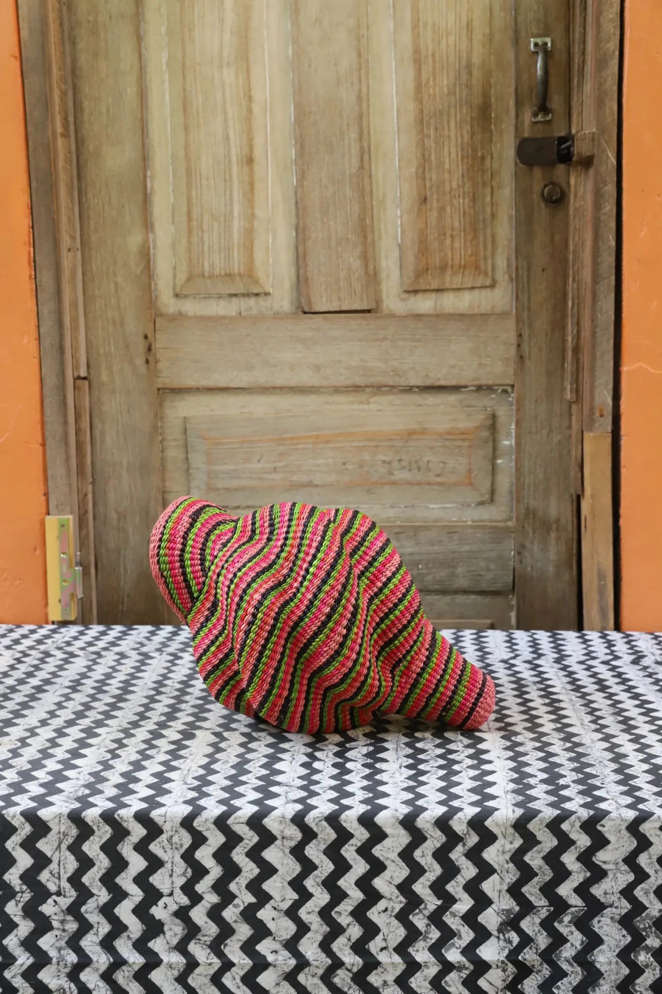 Colorful conch-shaped piece on a black and white cloth against a wooden door.