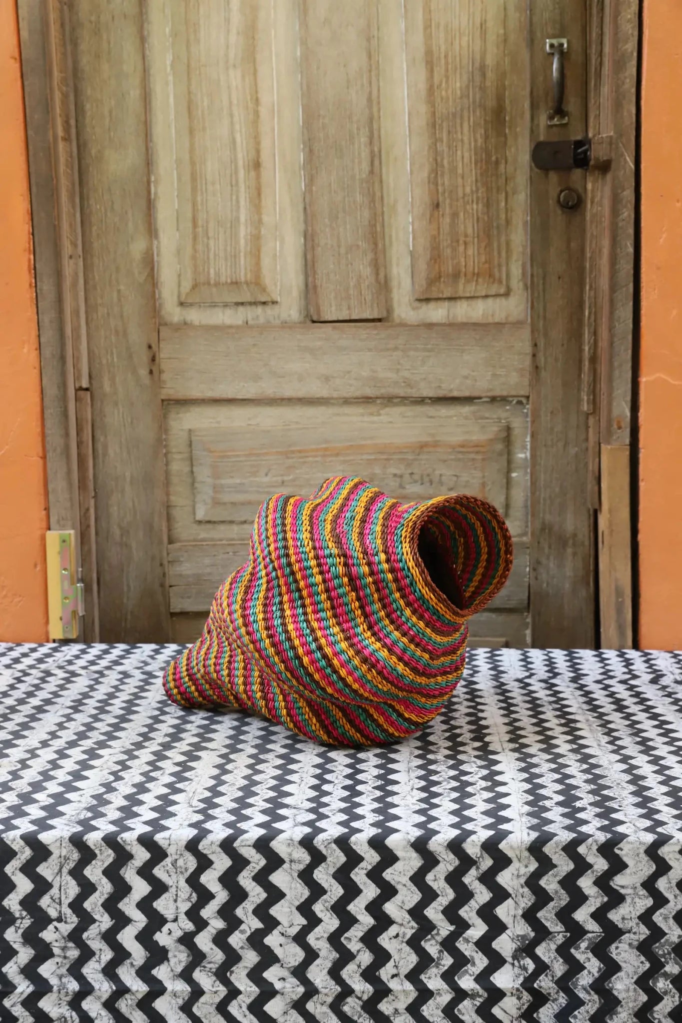 Colorful conch-shaped piece on a black and white cloth against a wooden door.