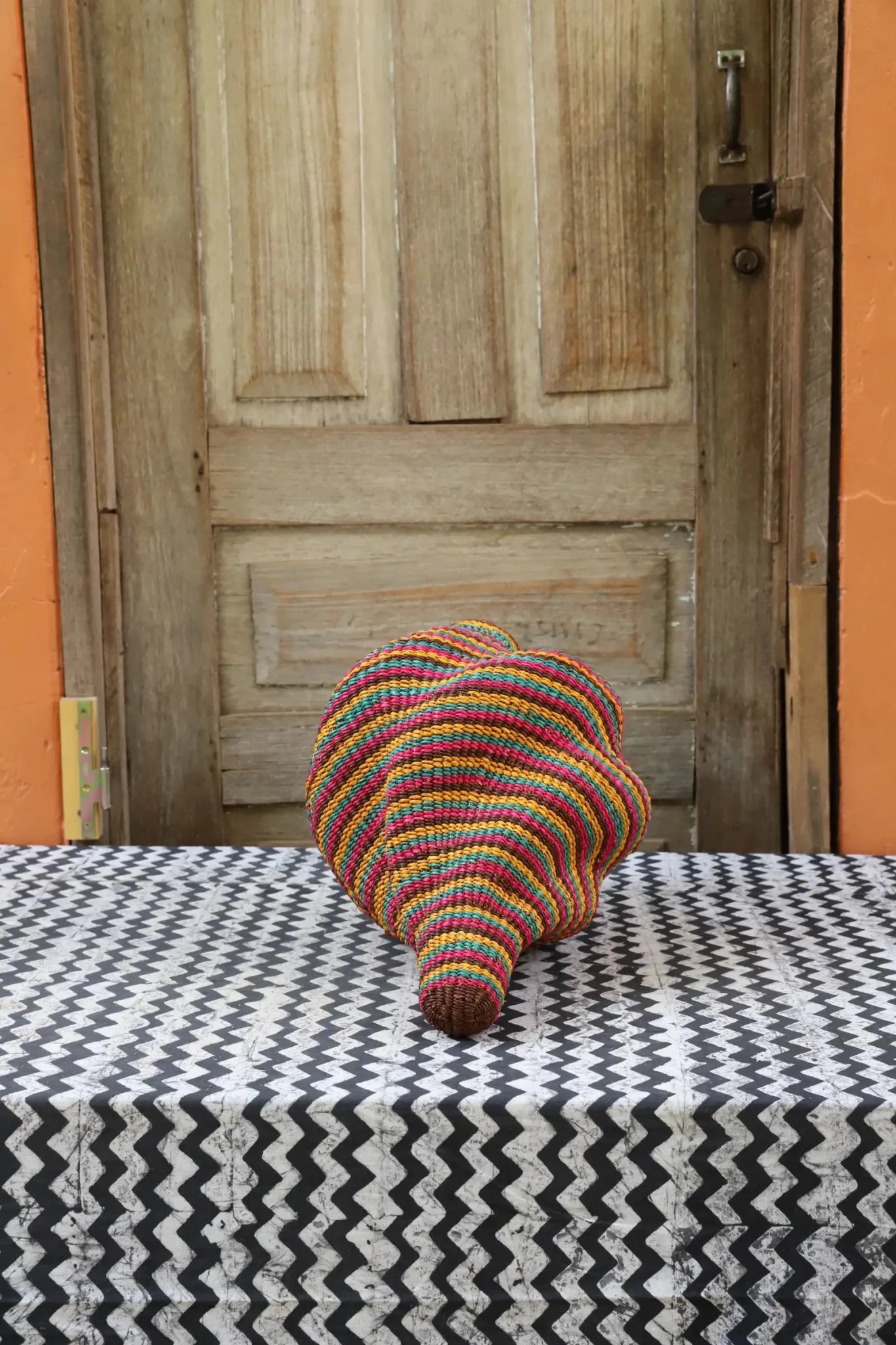 Woven conch piece on a black and white patterned surface with a wooden door in the background.