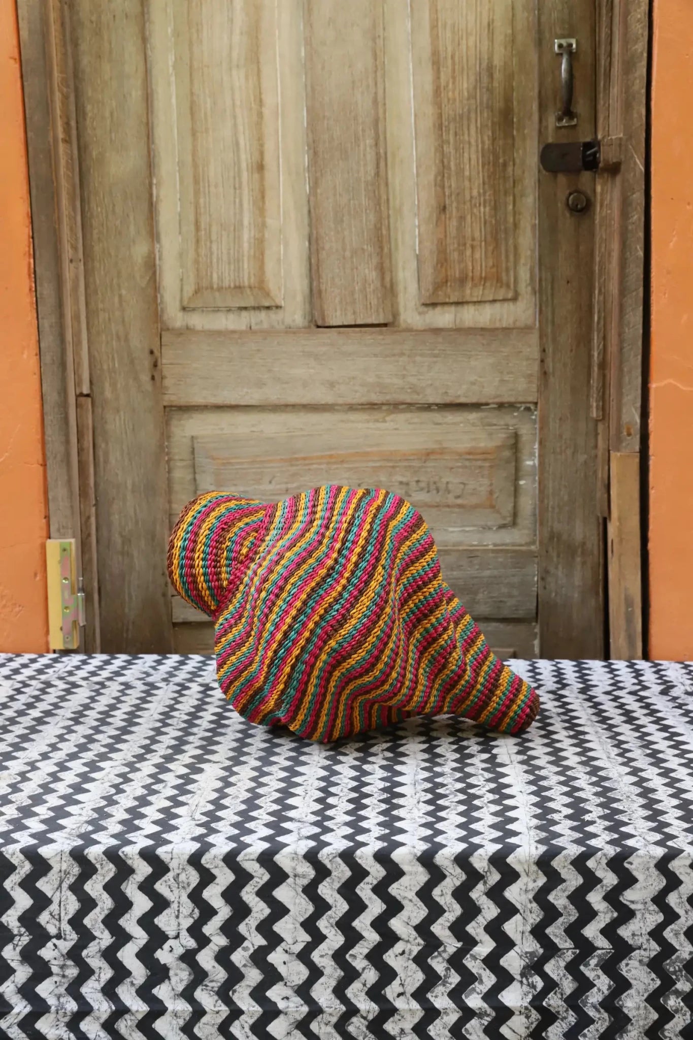 Woven conch piece on a black and white patterned surface with a wooden door in the background.
