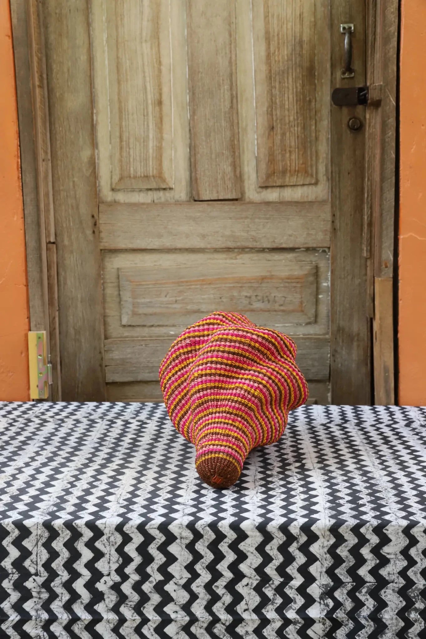 Woven conch piece on a black and white patterned surface with a wooden door in the background.