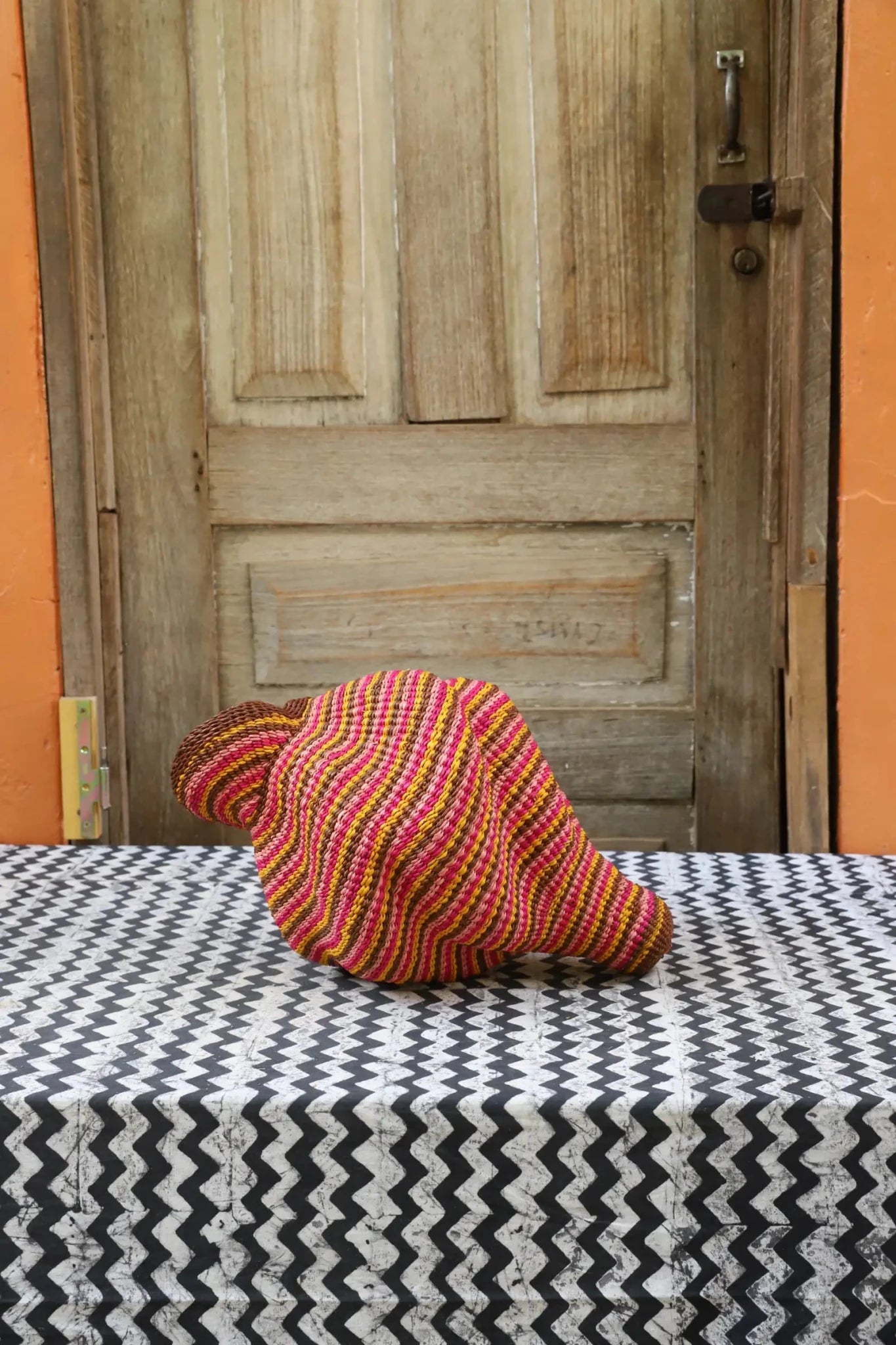 Woven conch piece on a black and white patterned surface with a wooden door in the background.
