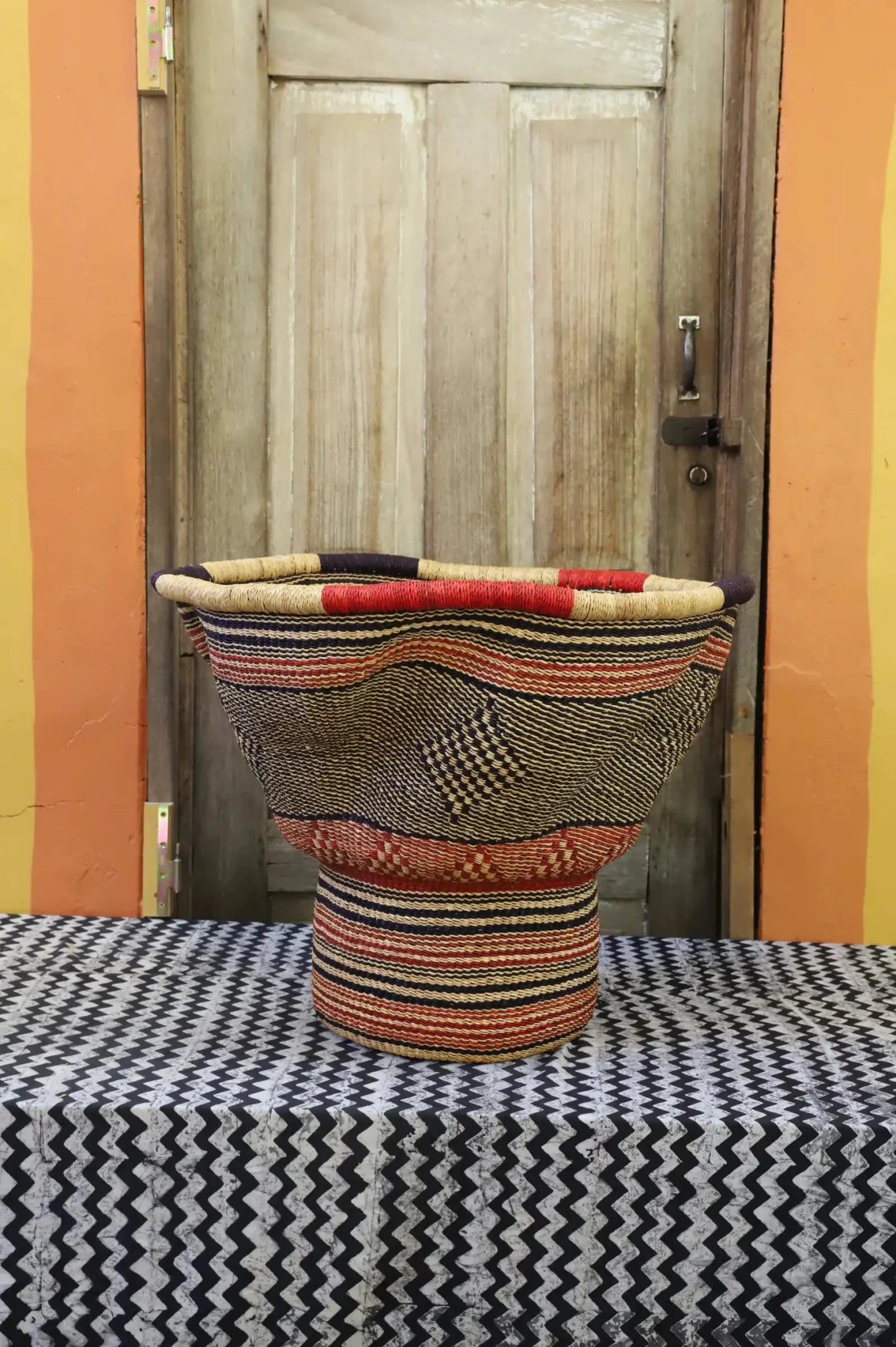 Decorative woven basket with stylish straw branching out on a black and white cloth against a wooden door.