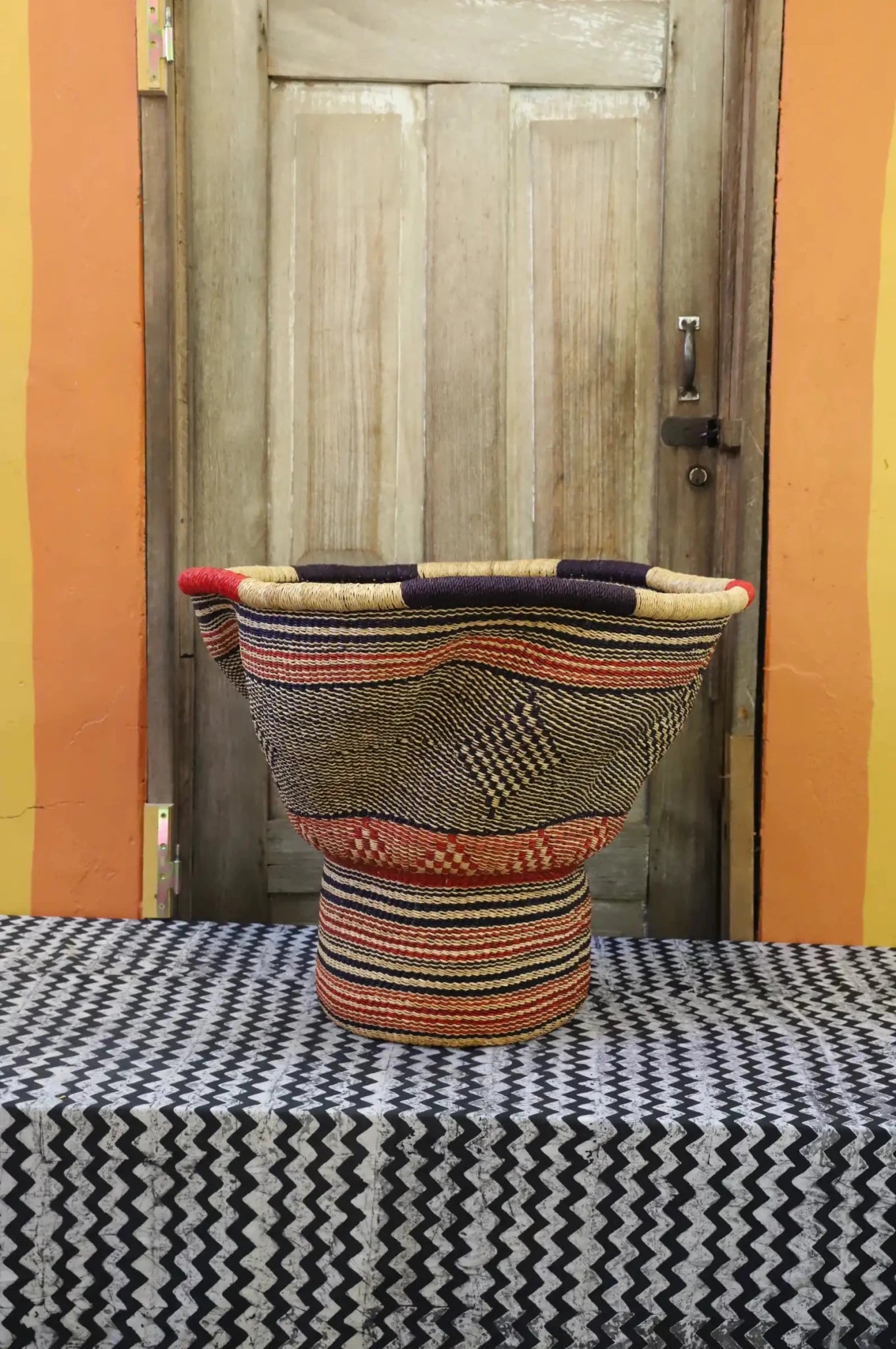 A patterned, handwoven piece sitting on a black and white cloth against a wooden door