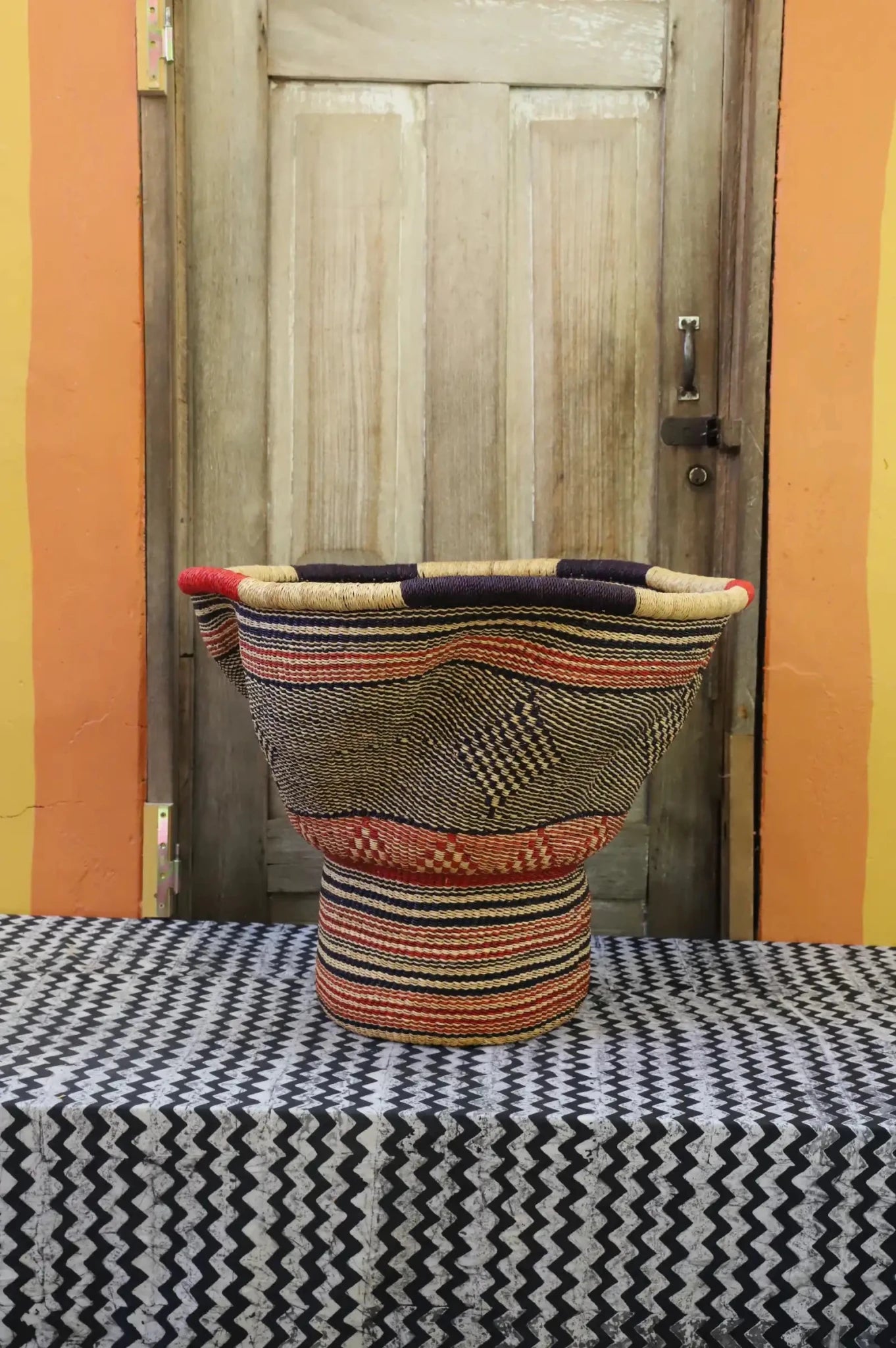 Decorative woven basket with stylish straw branching out on a black and white cloth against a wooden door.