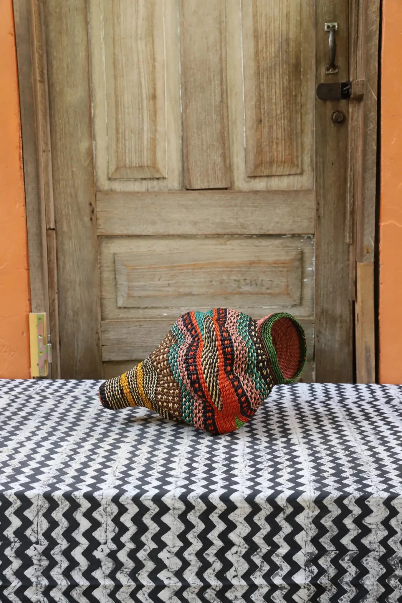 Colorful conch-shaped piece on a black and white cloth against a wooden door.