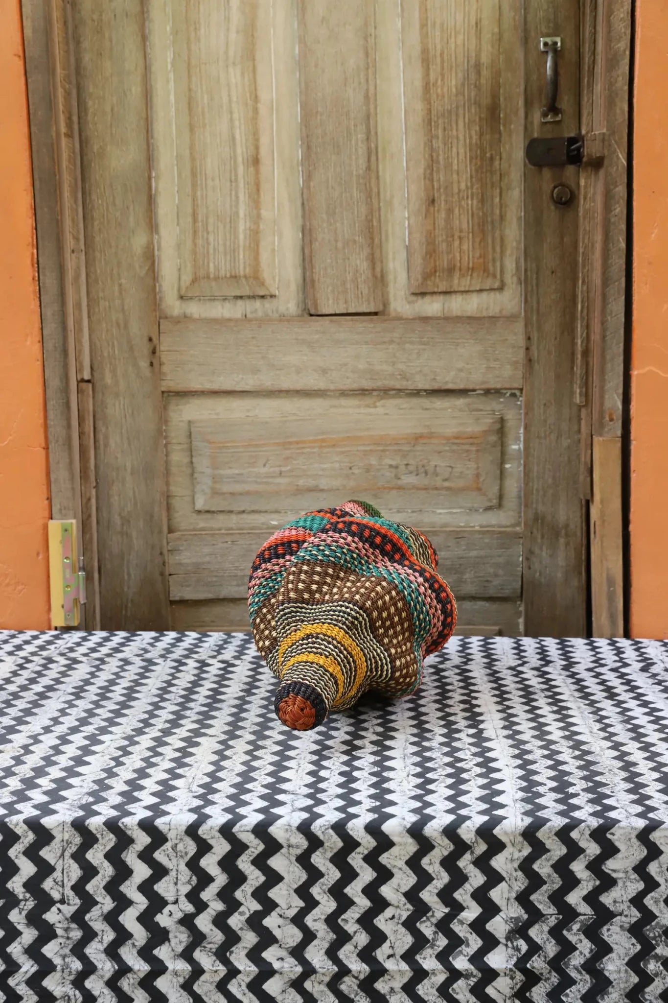 Woven conch piece on a black and white patterned surface with a wooden door in the background.