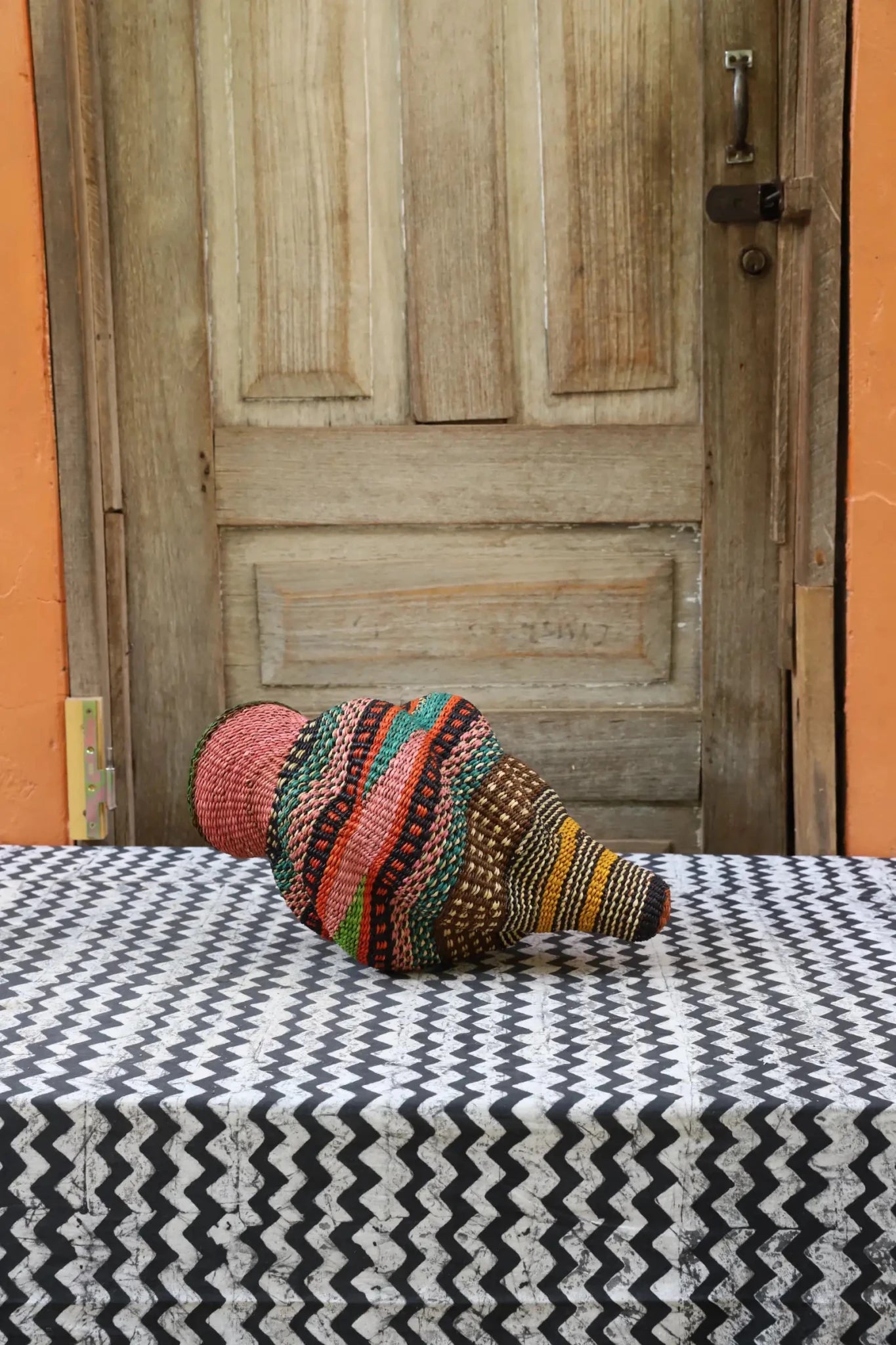 Woven conch piece on a black and white patterned surface with a wooden door in the background.