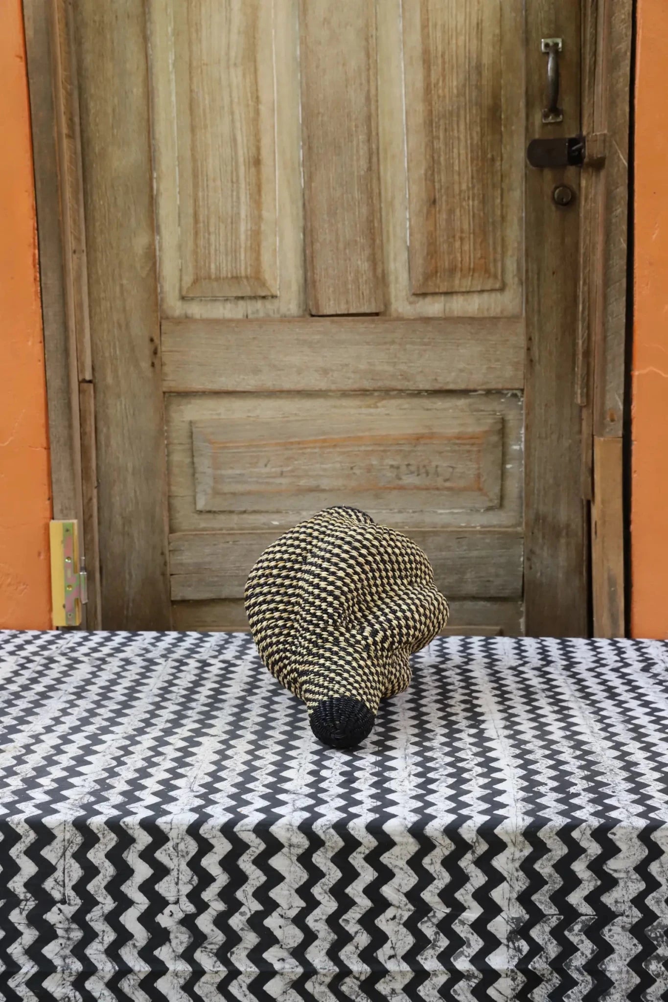 Woven conch piece on a black and white patterned surface with a wooden door in the background.