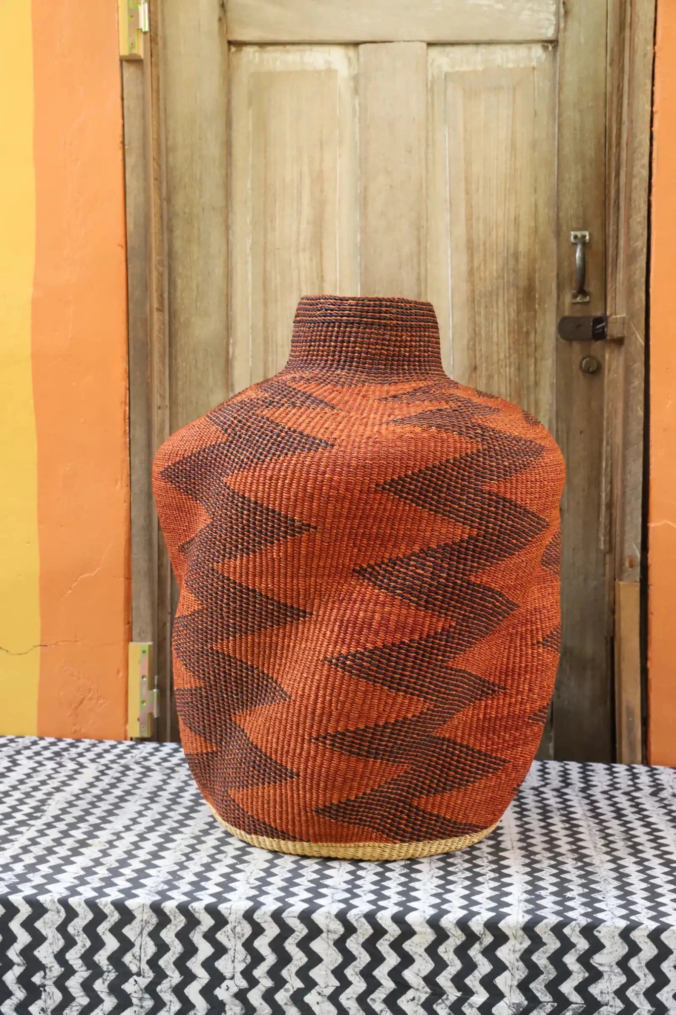 Curvy, handwoven décor piece on a black and white cloth against a wooden door.
