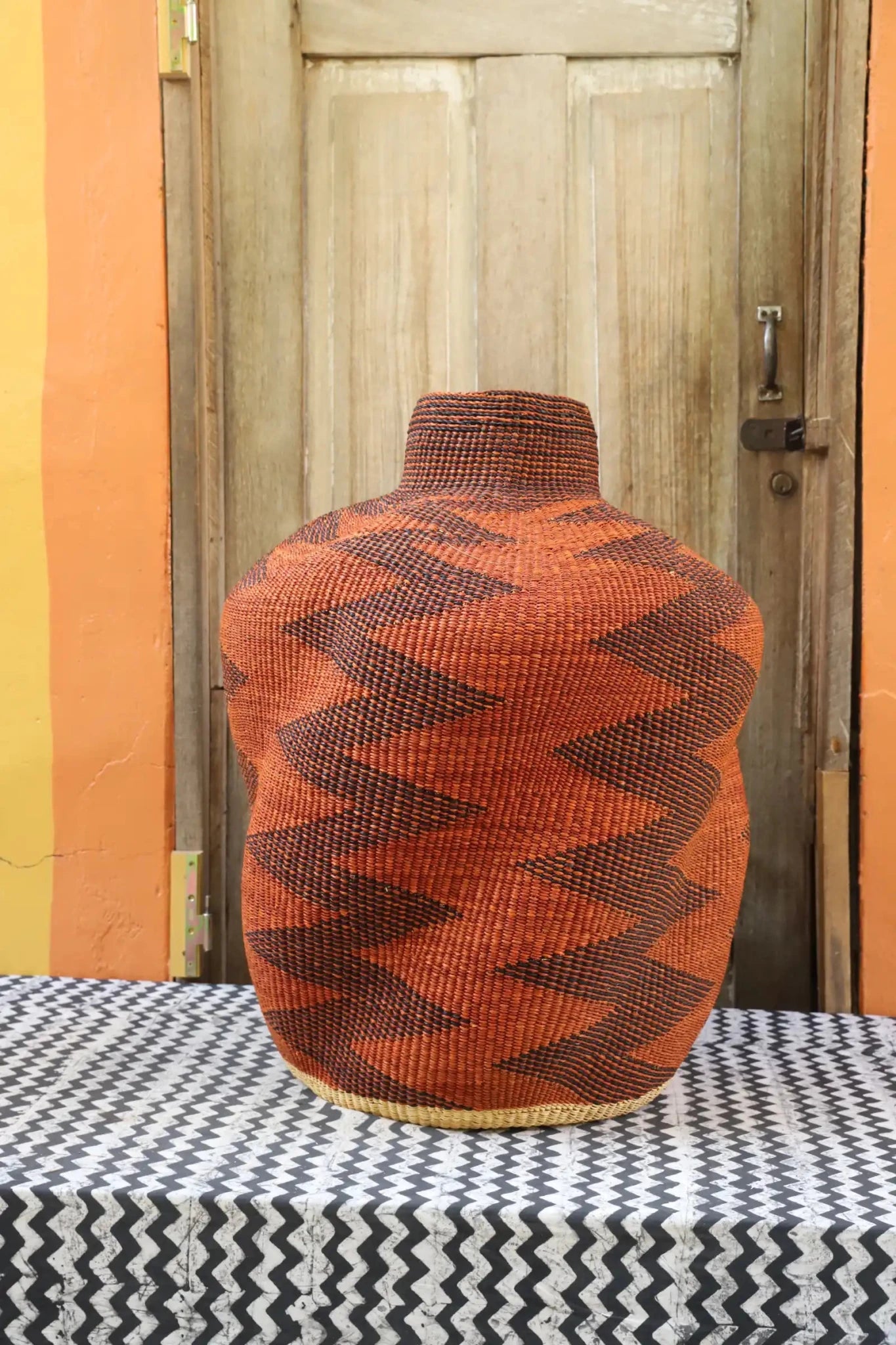 Curvy, handwoven décor piece on a black and white cloth against a wooden door.