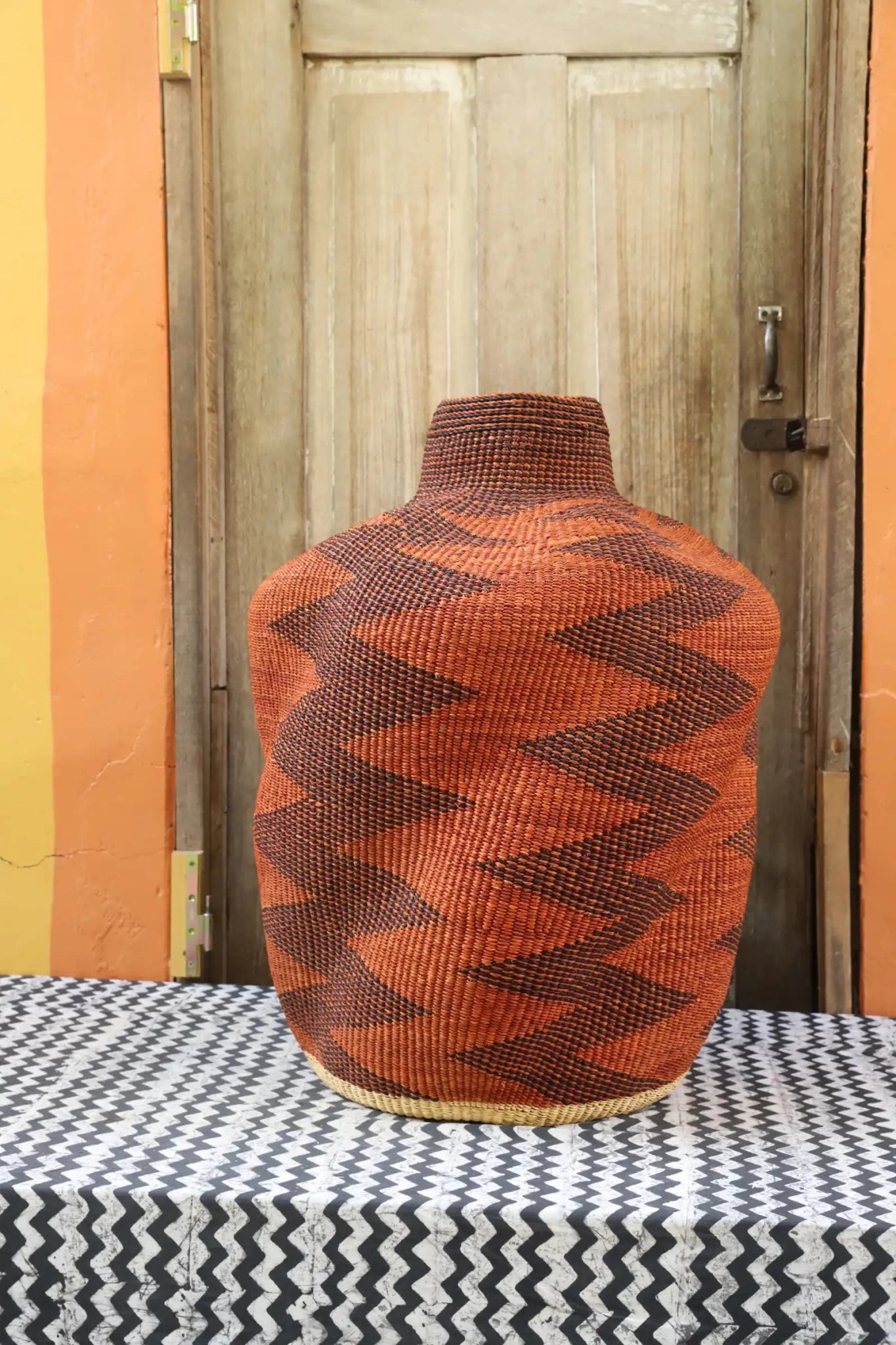 Curvy, handwoven piece on a black and white cloth against a wooden door.