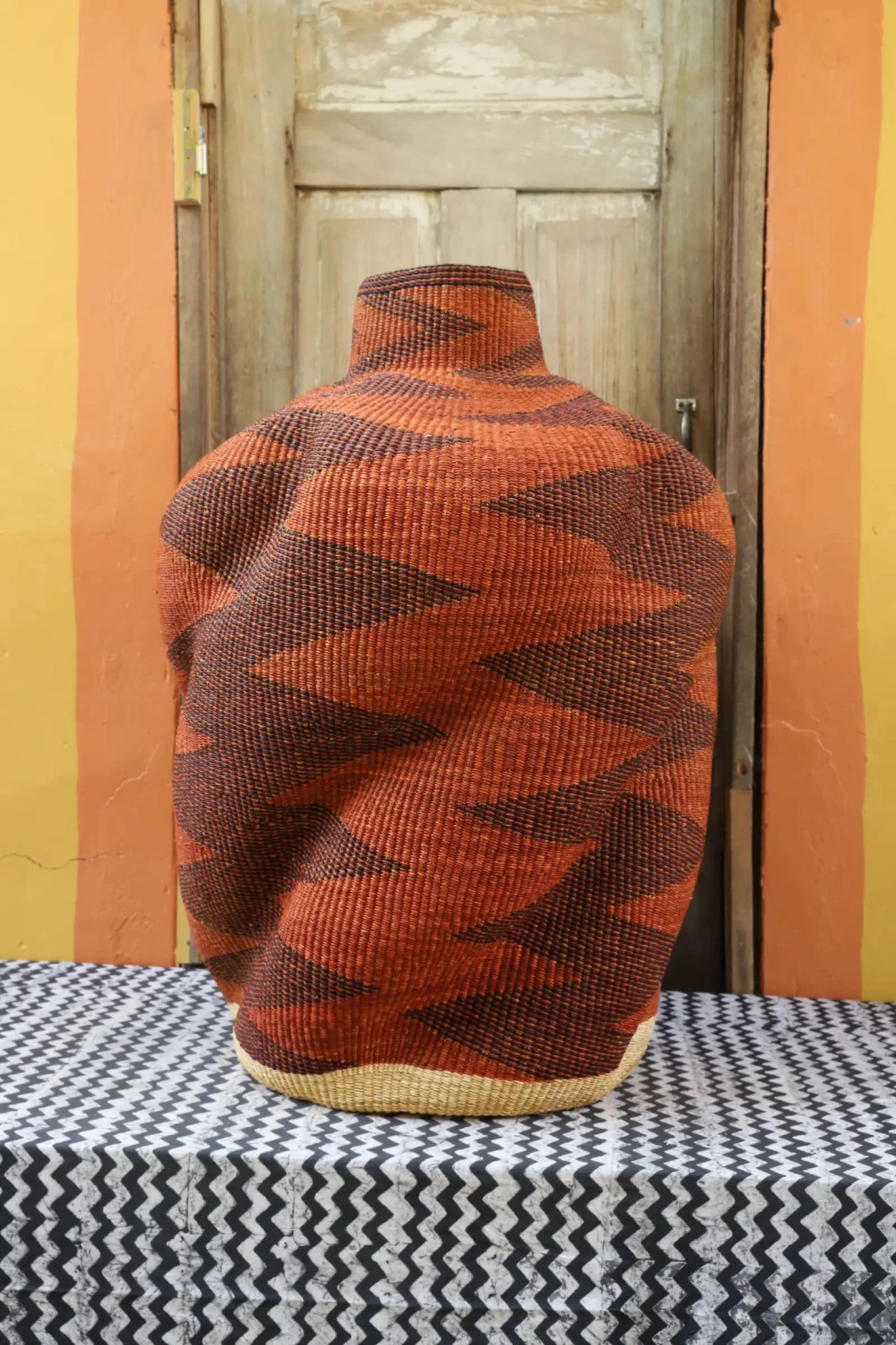 Curvy, handwoven piece on a black and white cloth against a wooden door.