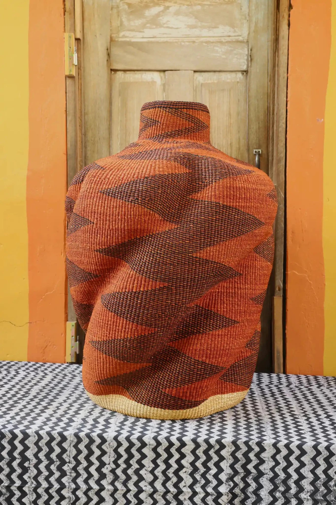 Curvy, handwoven décor piece on a black and white cloth against a wooden door.