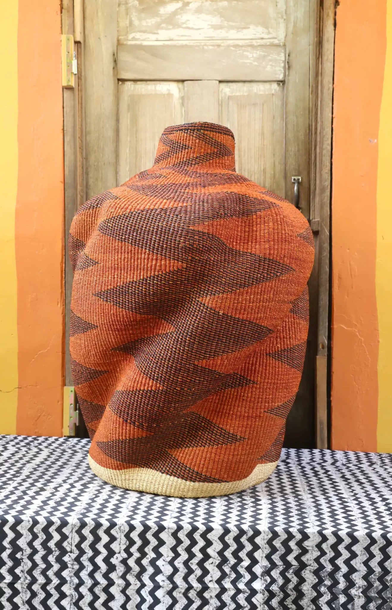 Curvy, handwoven décor piece on a black and white cloth against a wooden door.