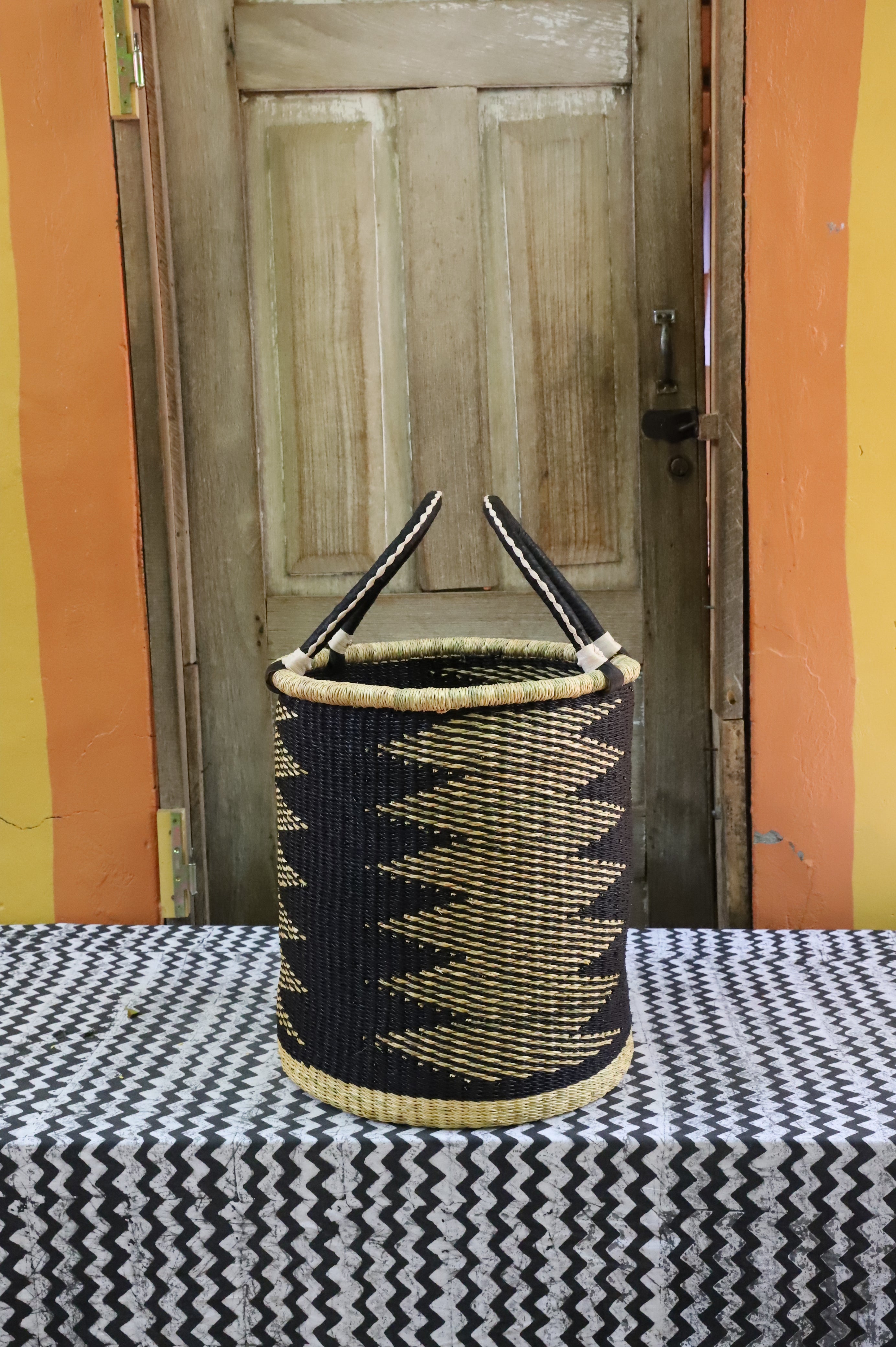 Open laundry basket in black and natural straw zigzag weave with beaded handle ends, styled on a chevron cloth.