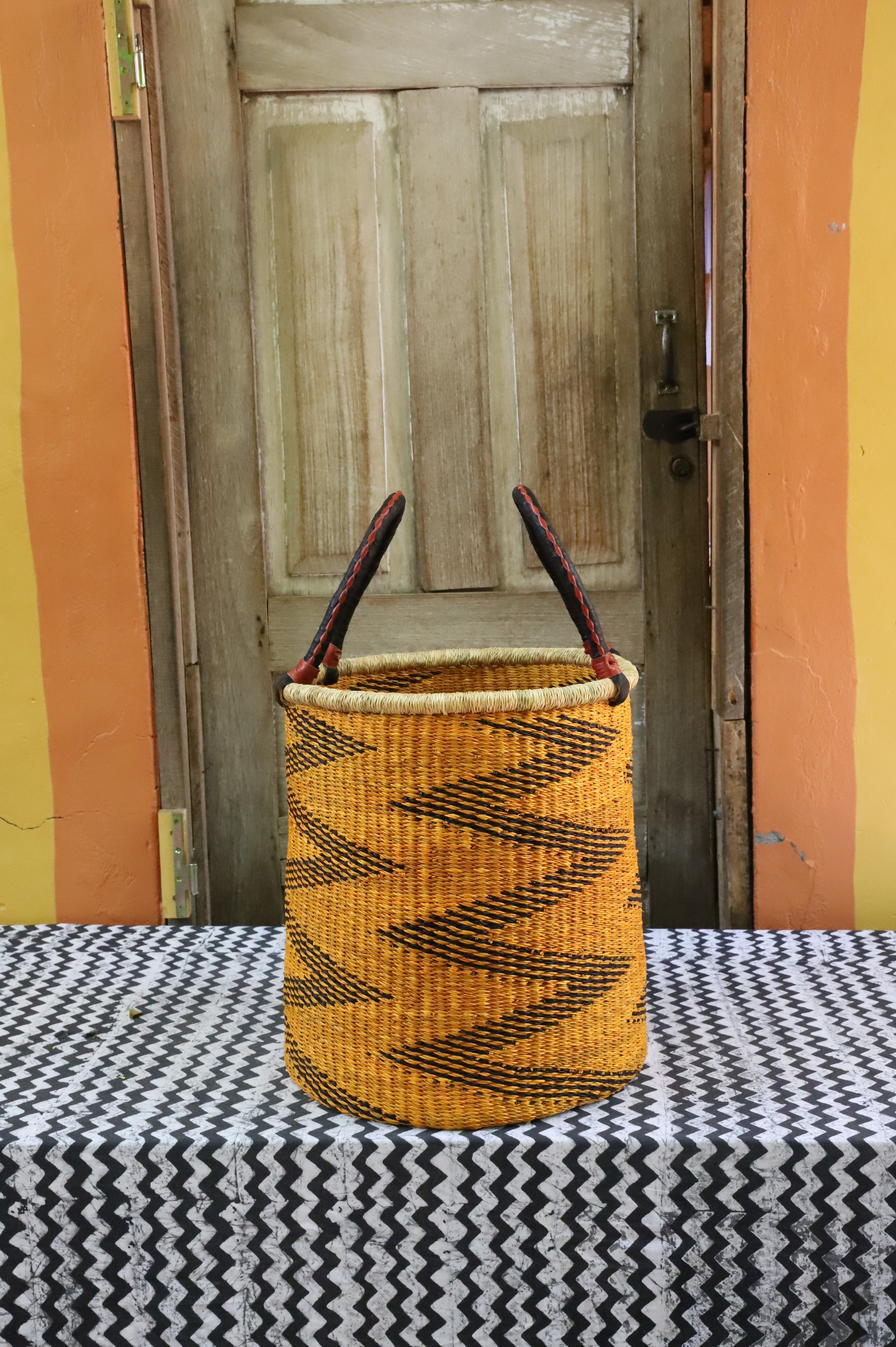 Open laundry basket in mustard and black zigzag weave with arched handles, styled on a chevron cloth.
