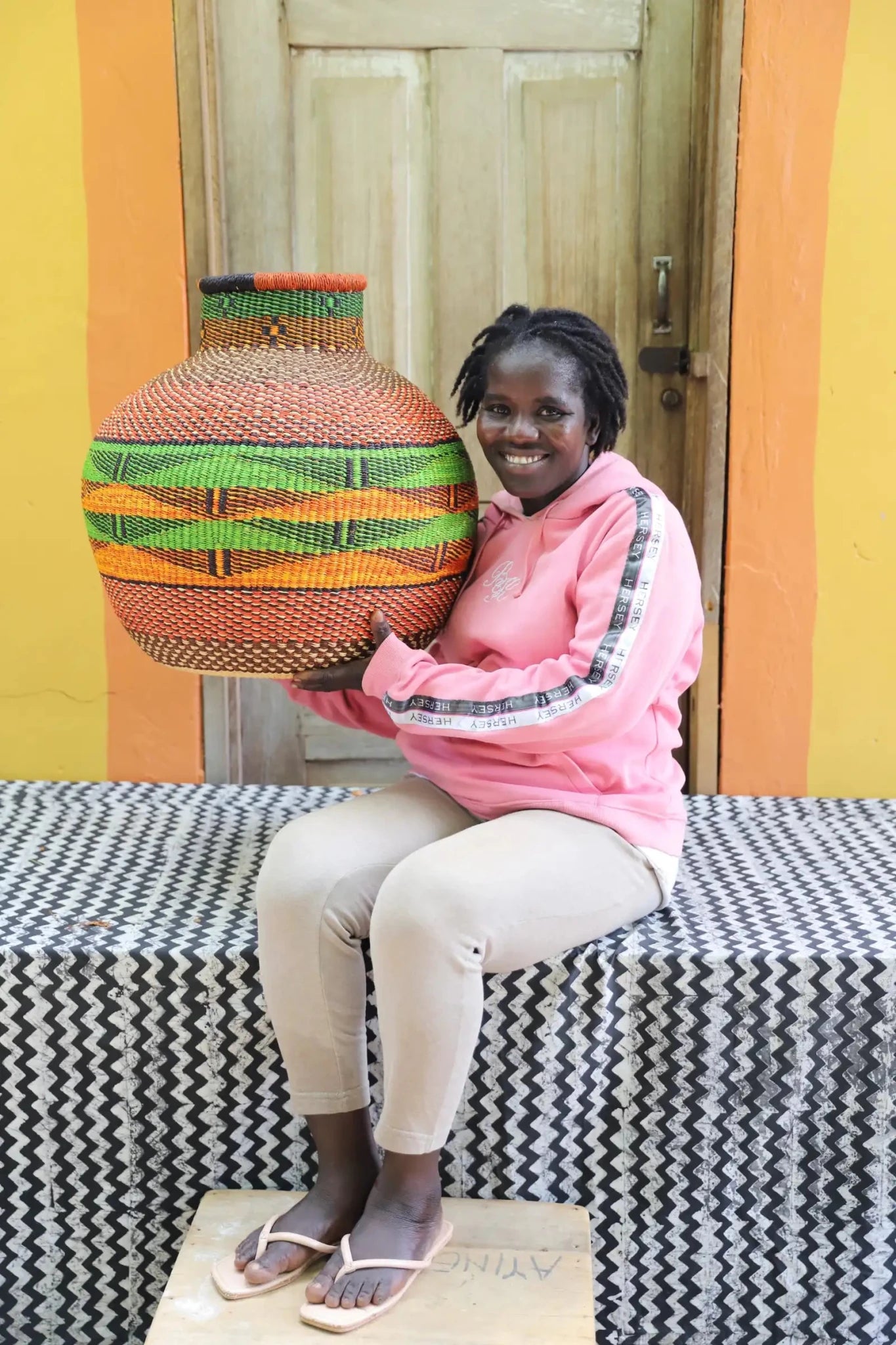 Decorative handwoven basket with colorful patterns on a black and white cloth against a wooden door.