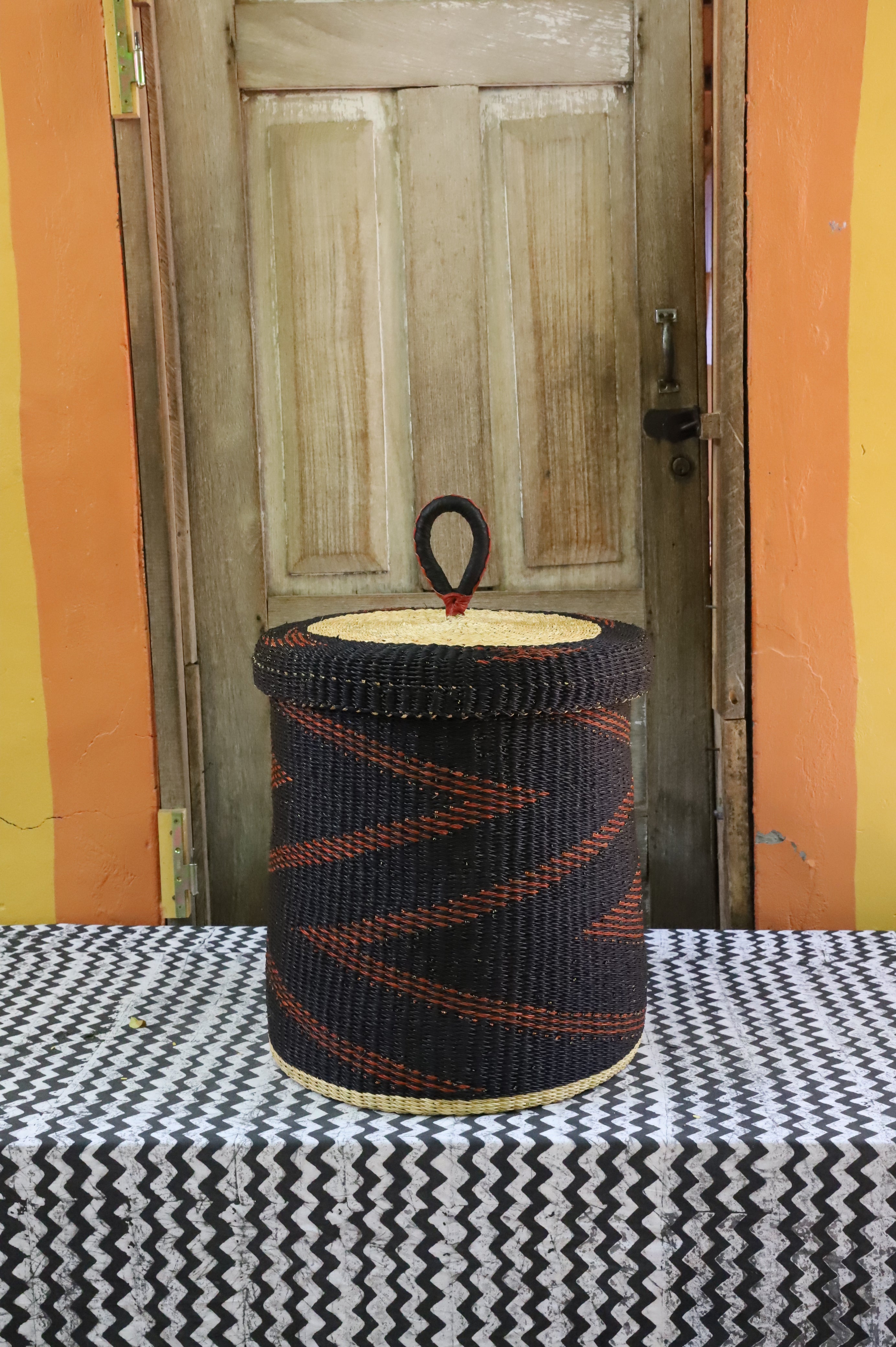 Lidded laundry basket in dark brown elephant grass with a rust zigzag weave, styled on a chevron cloth.