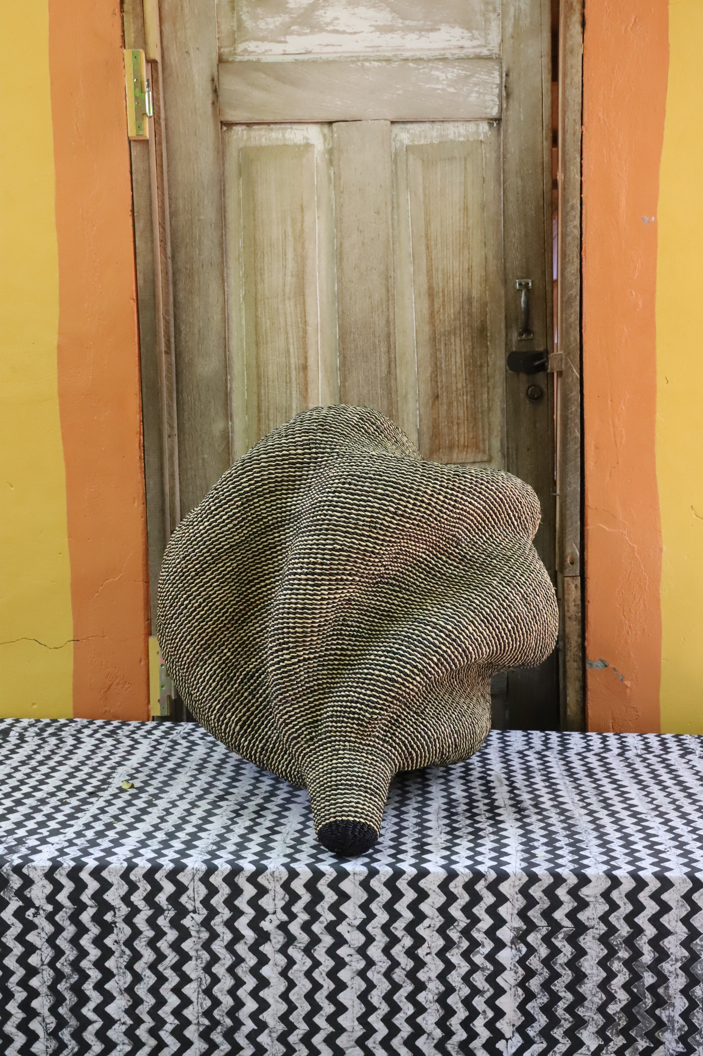 Densely coiled spiral Bolga basket in natural straw, textured woven surface, styled by a wooden door.