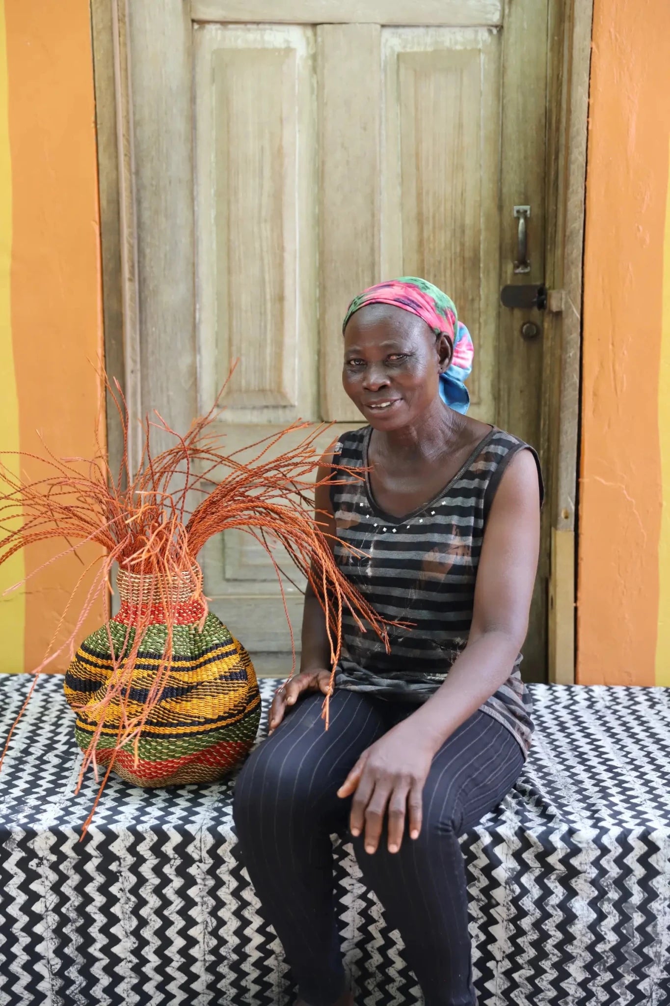 A colorful, handwoven piece sitting on a black and white cloth with decorative straw branching out. 