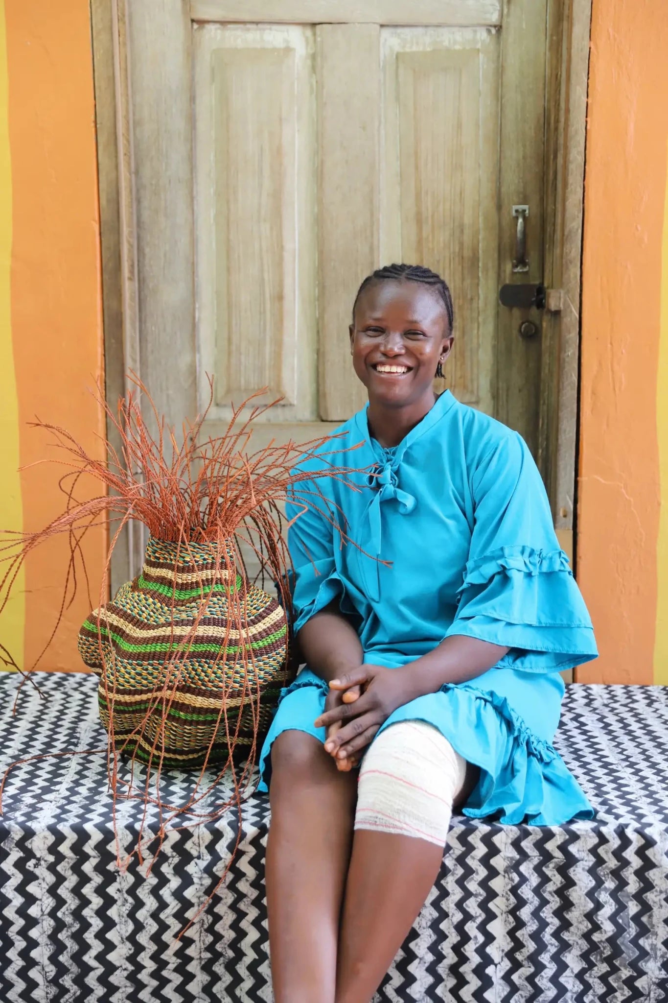 A colorful, handwoven piece sitting on a black and white cloth with decorative straw branching out. 