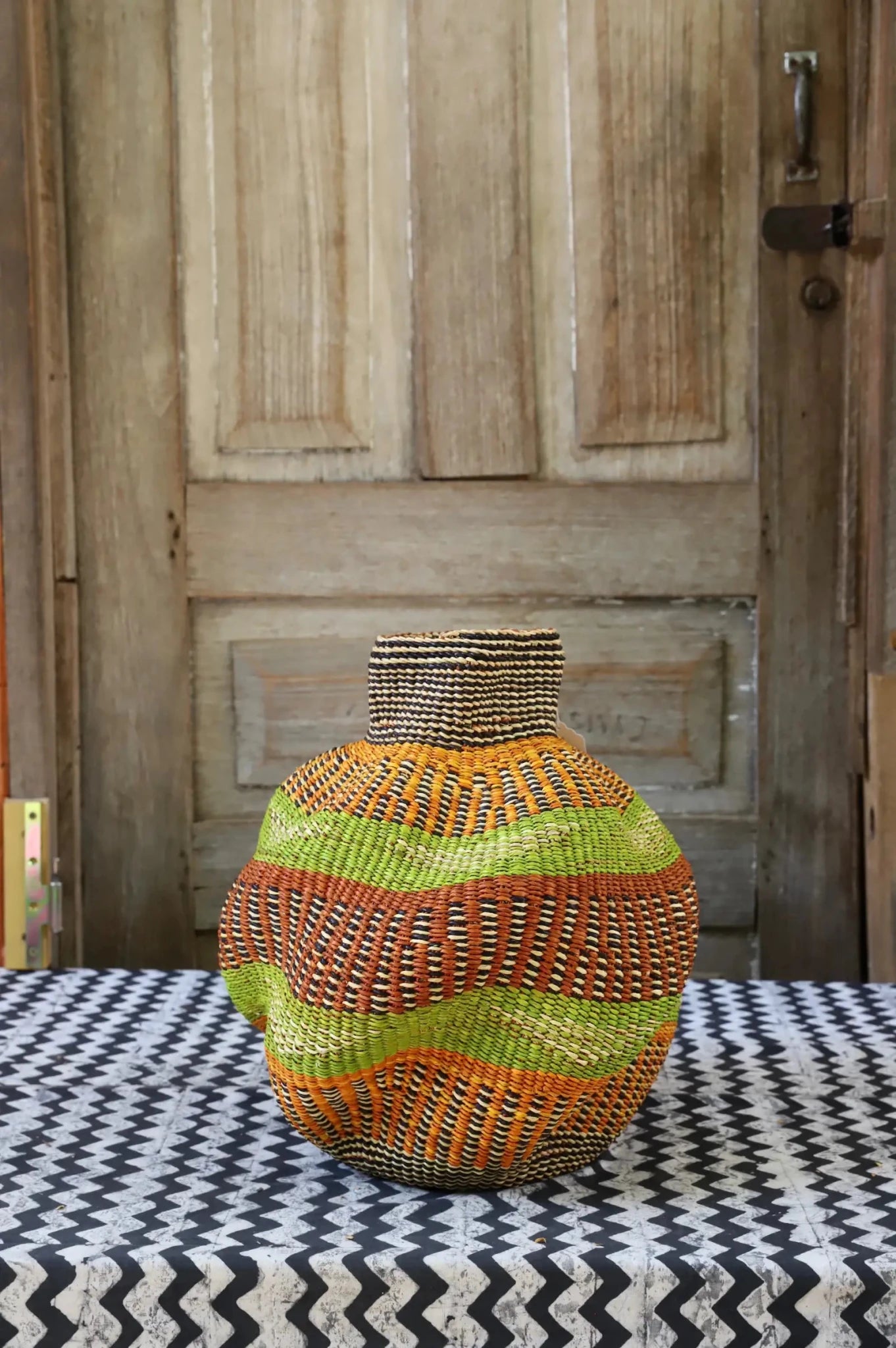 A colorful, handwoven piece with decorative curves sitting on a black and white cloth against a wooden door
