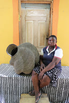 Large spiral-form Bolga basket in natural straw, shown beside a seated person for scale.