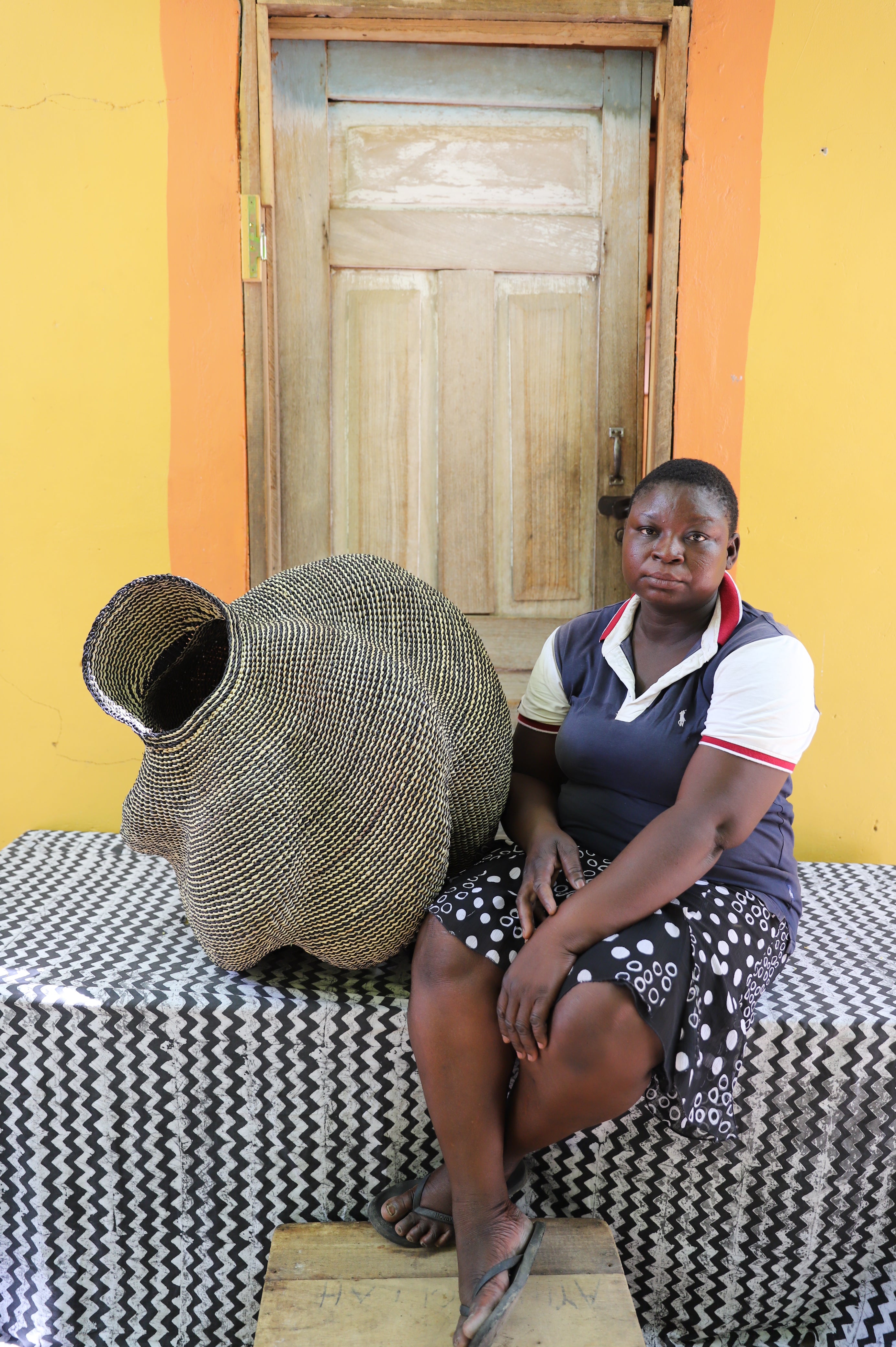 Large spiral-form Bolga basket in natural straw, shown beside a seated person for scale.