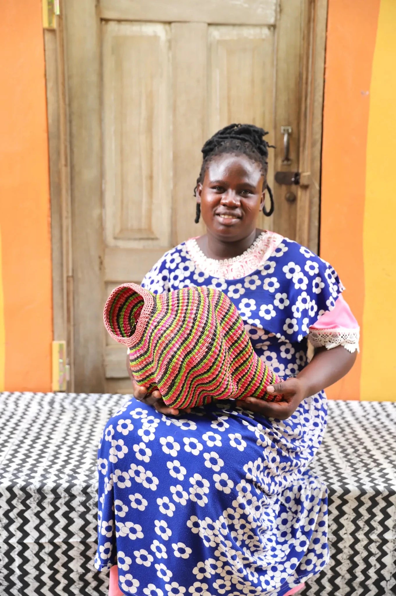 Woman holding a woven conch piece on a black and white patterned surface with a wooden door in the background.